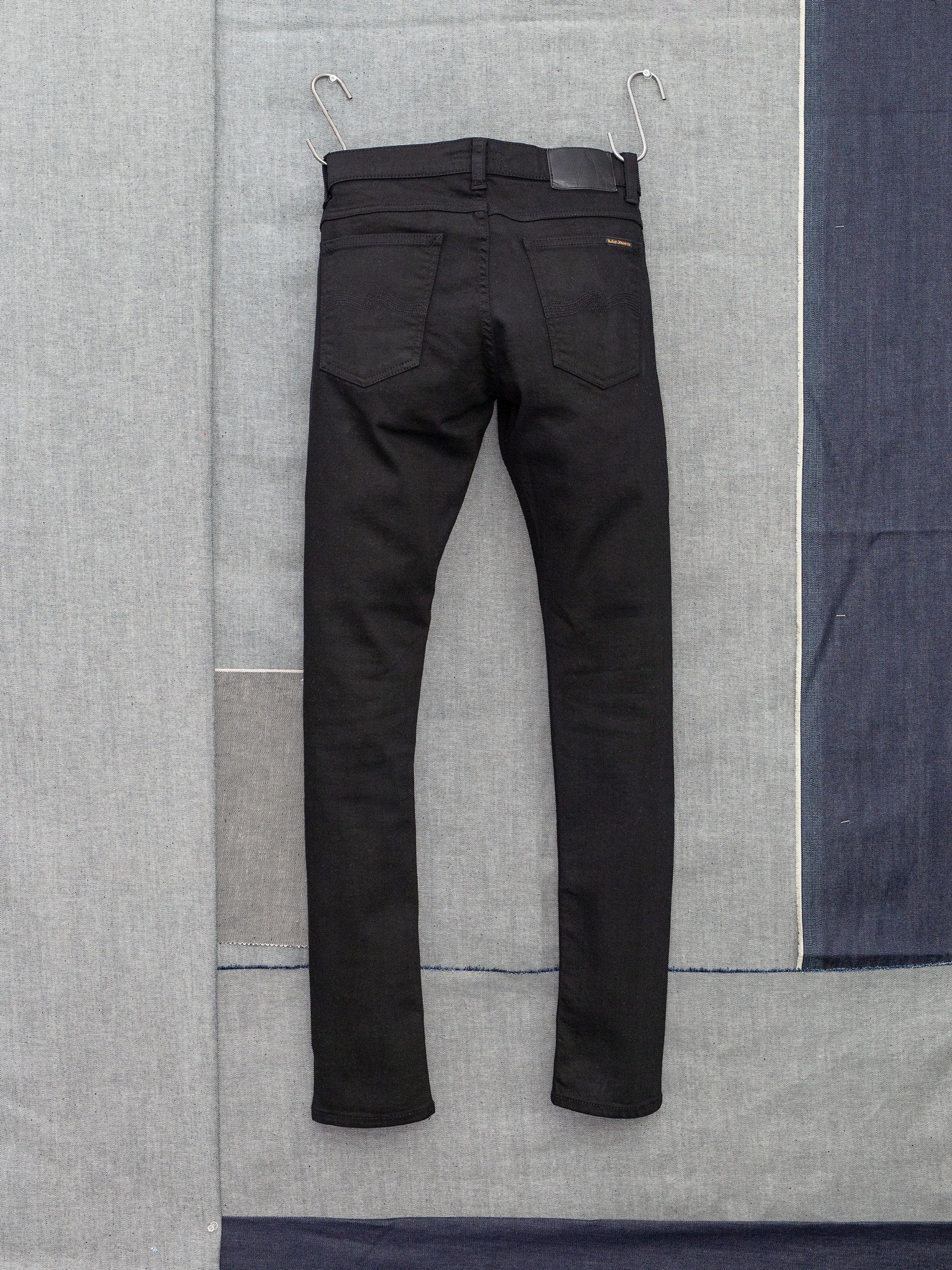 Nudie Jeans Tight Terry Everblack, men's tight fit jeans, shown from the back hanging against a denim backdrop.