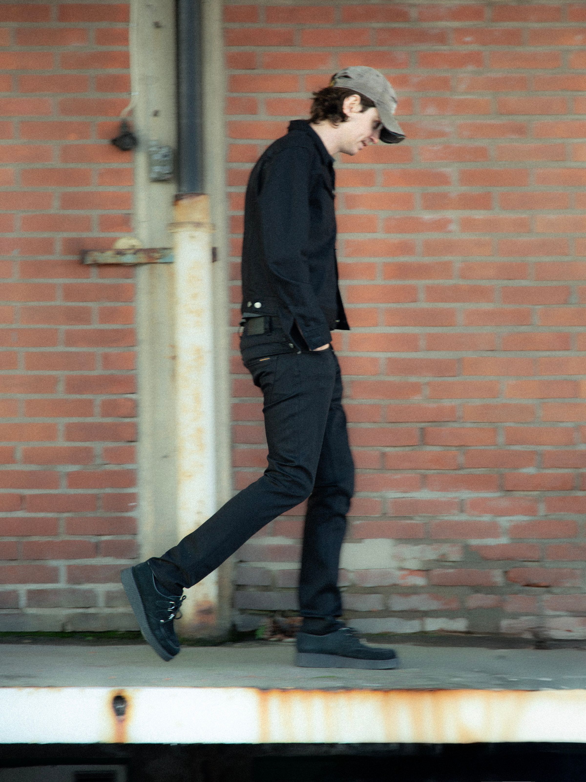 Nudie Jeans Grim Tim Dry Everblack, men's slim fit jeans shown on a model from the side while walking.