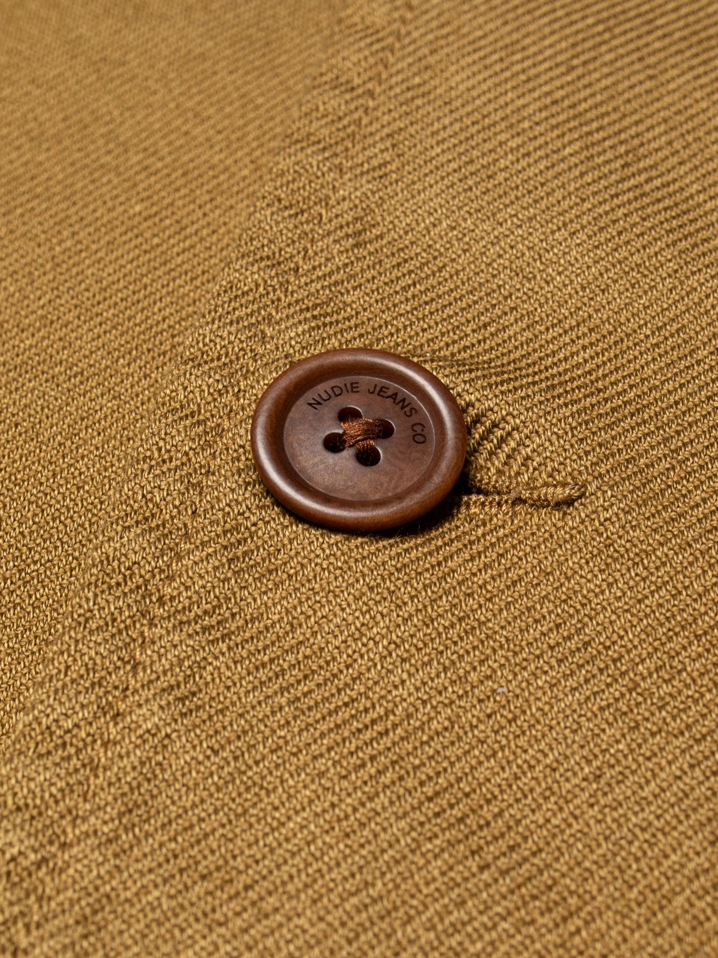 Nudie Jeans Barney Worker Jacket in Brown Olive, Nahaufnahme des gebrandeten Knopfes und des Bio-Baumwoll-Twill-Stoffs.