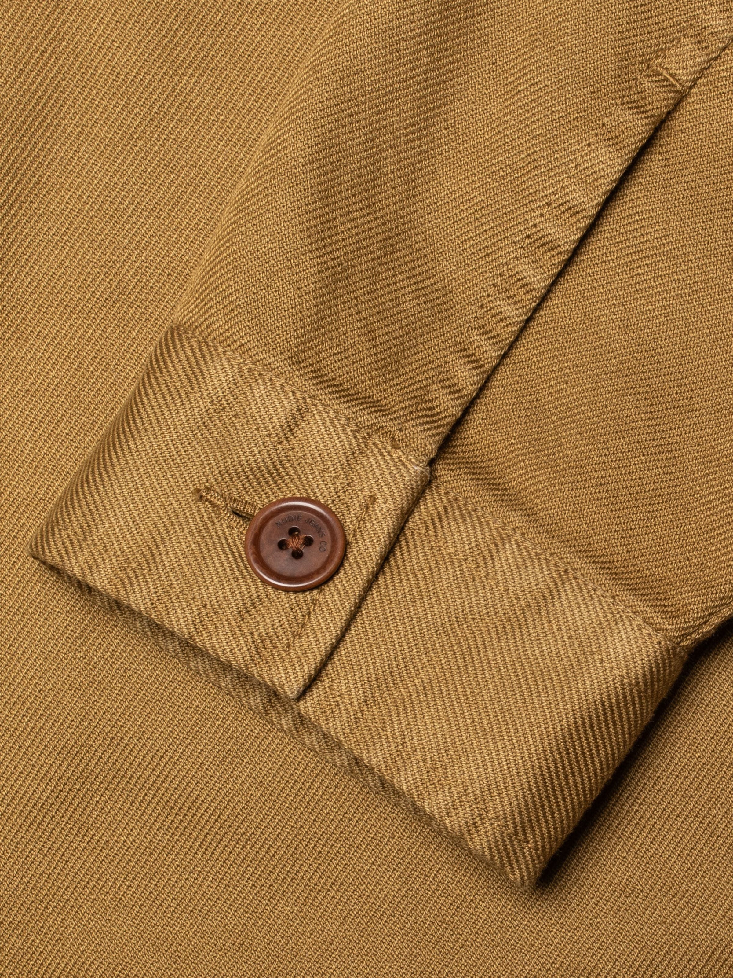 Nudie Jeans Barney Worker Jacket in Braun-Olive, Nahaufnahme mit Detail am Ärmelknopf und der Struktur des Baumwolltwills.