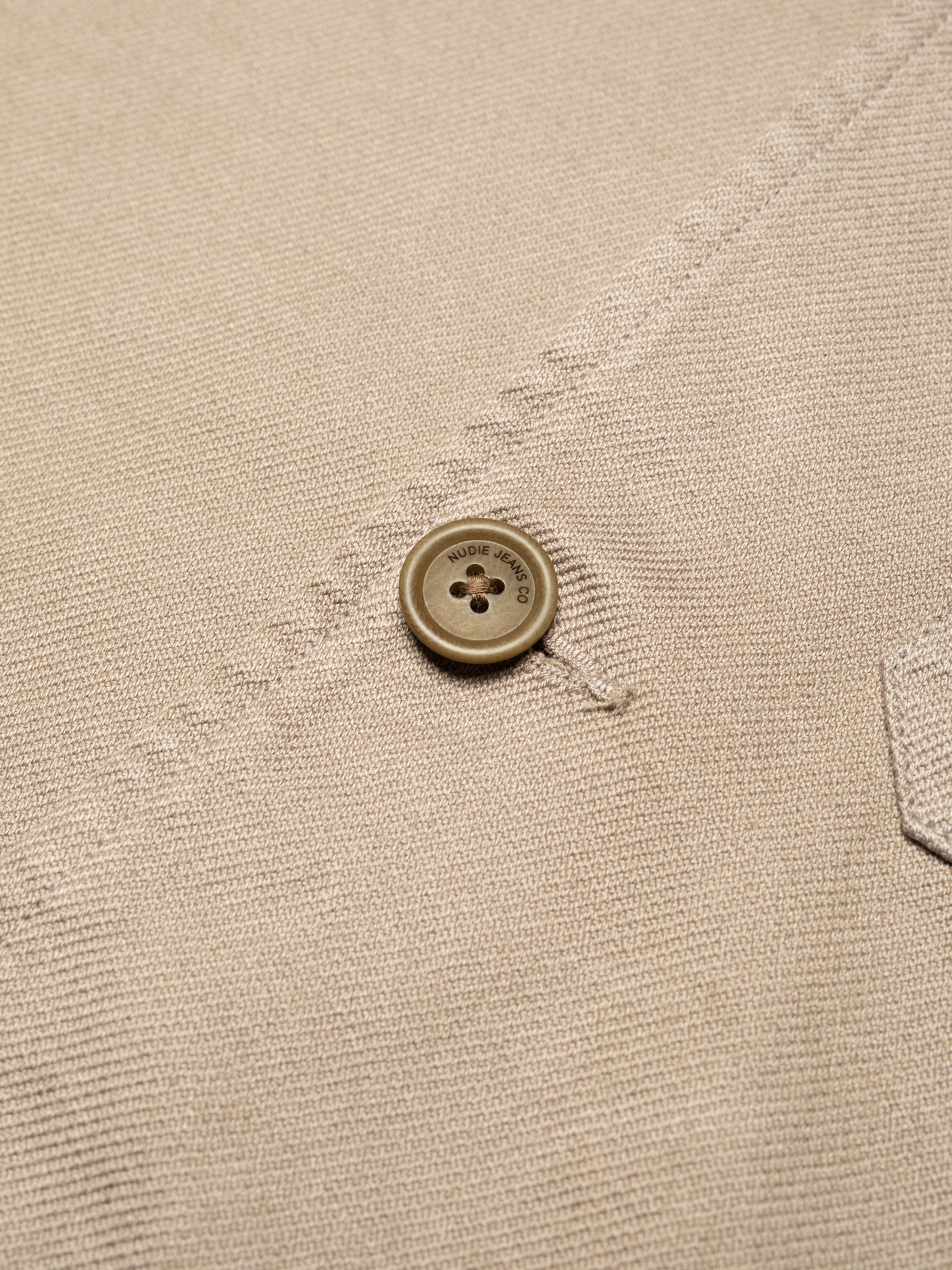 Nudie Jeans Barney Worker Jacket in Mud, a close-up of an engraved button showing the Nudie Jeans Co brand name.