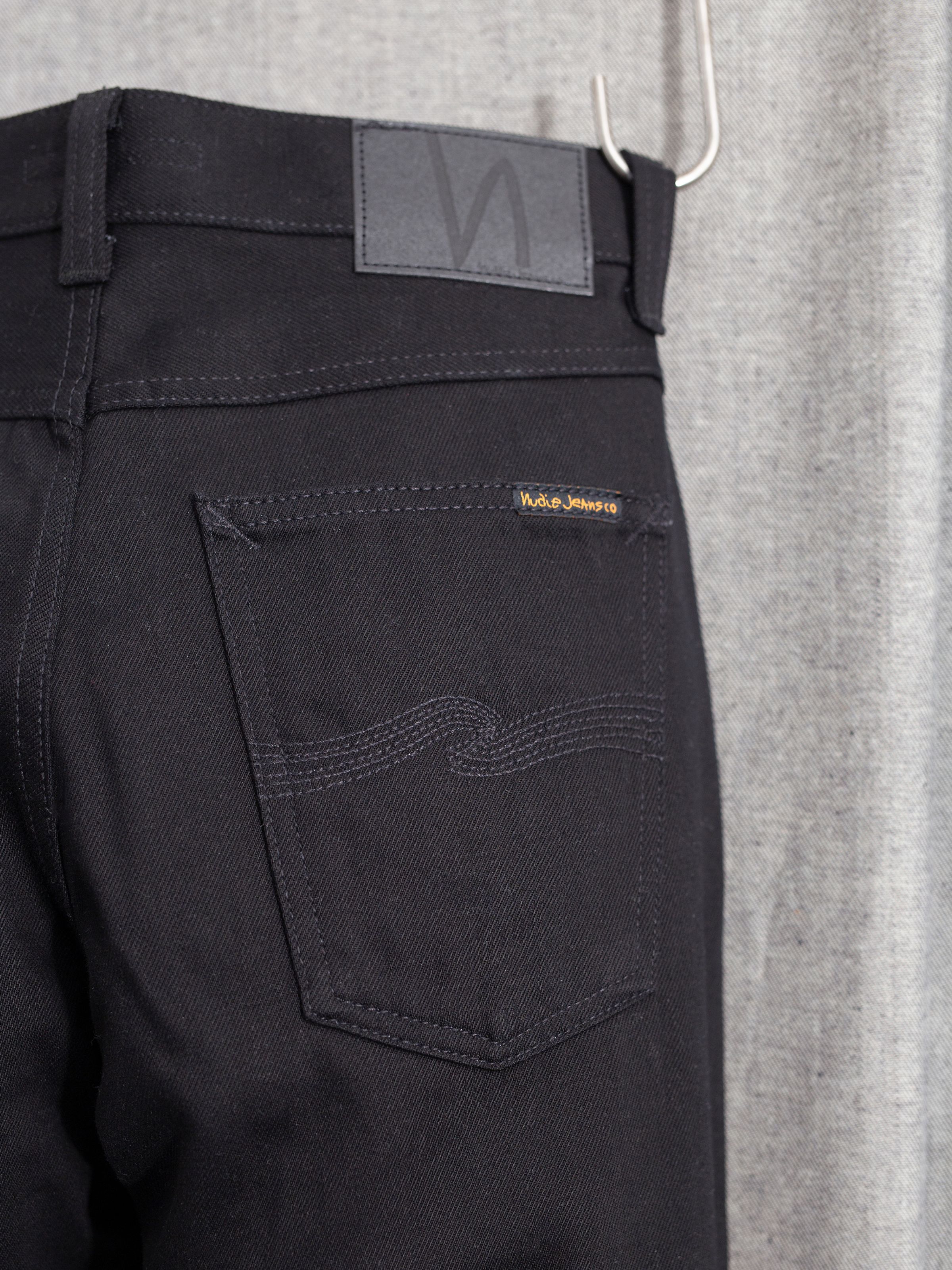 Nudie Jeans Steady Eddie II Dry Everblack, men's regular tapered fit jeans, close-up of the back pocket and Jacron patch.