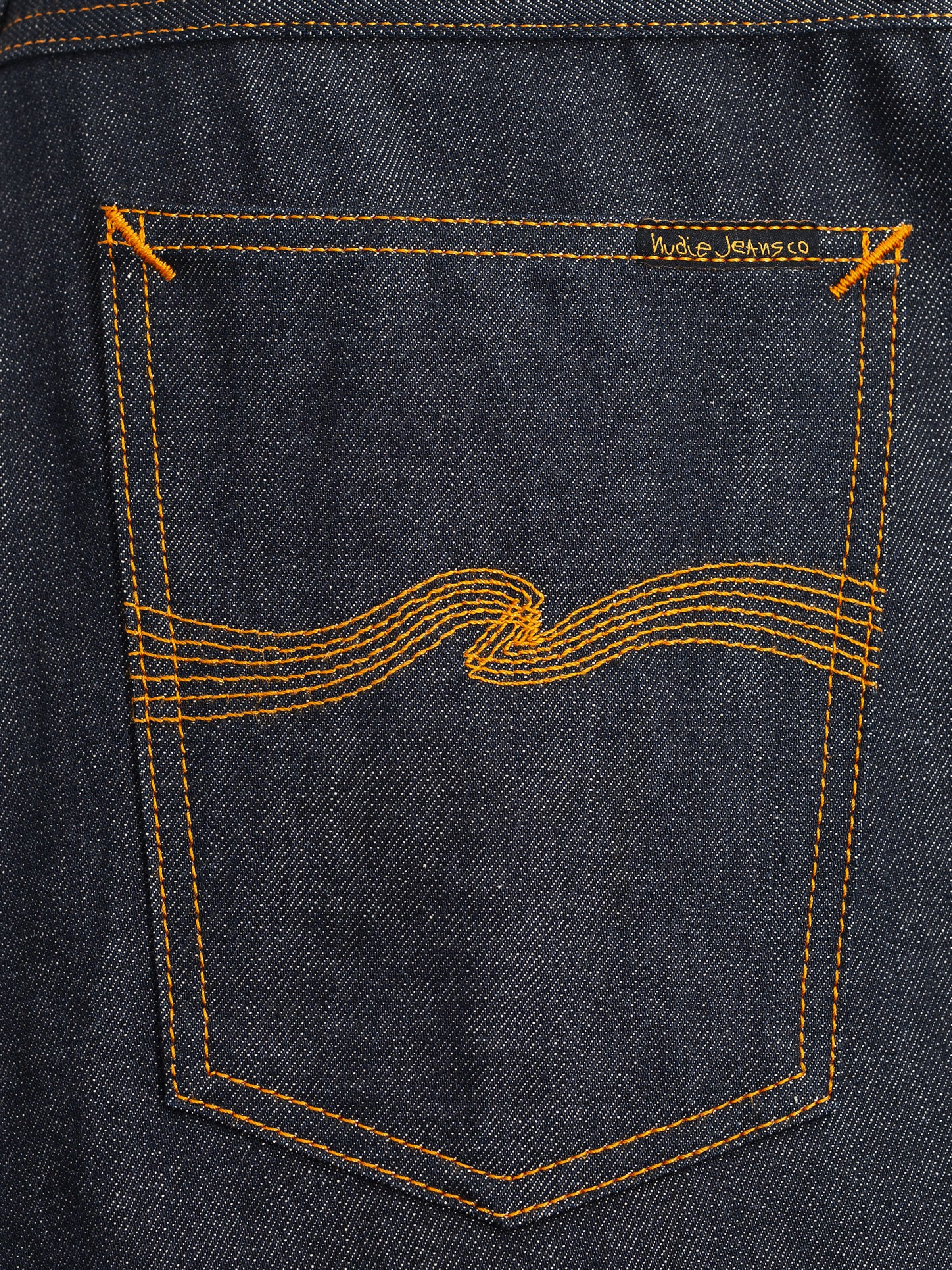 Nudie Jeans Gritty Jackson Dry Selvage, close-up of the back pocket with orange embroidery and rigid selvedge denim texture.