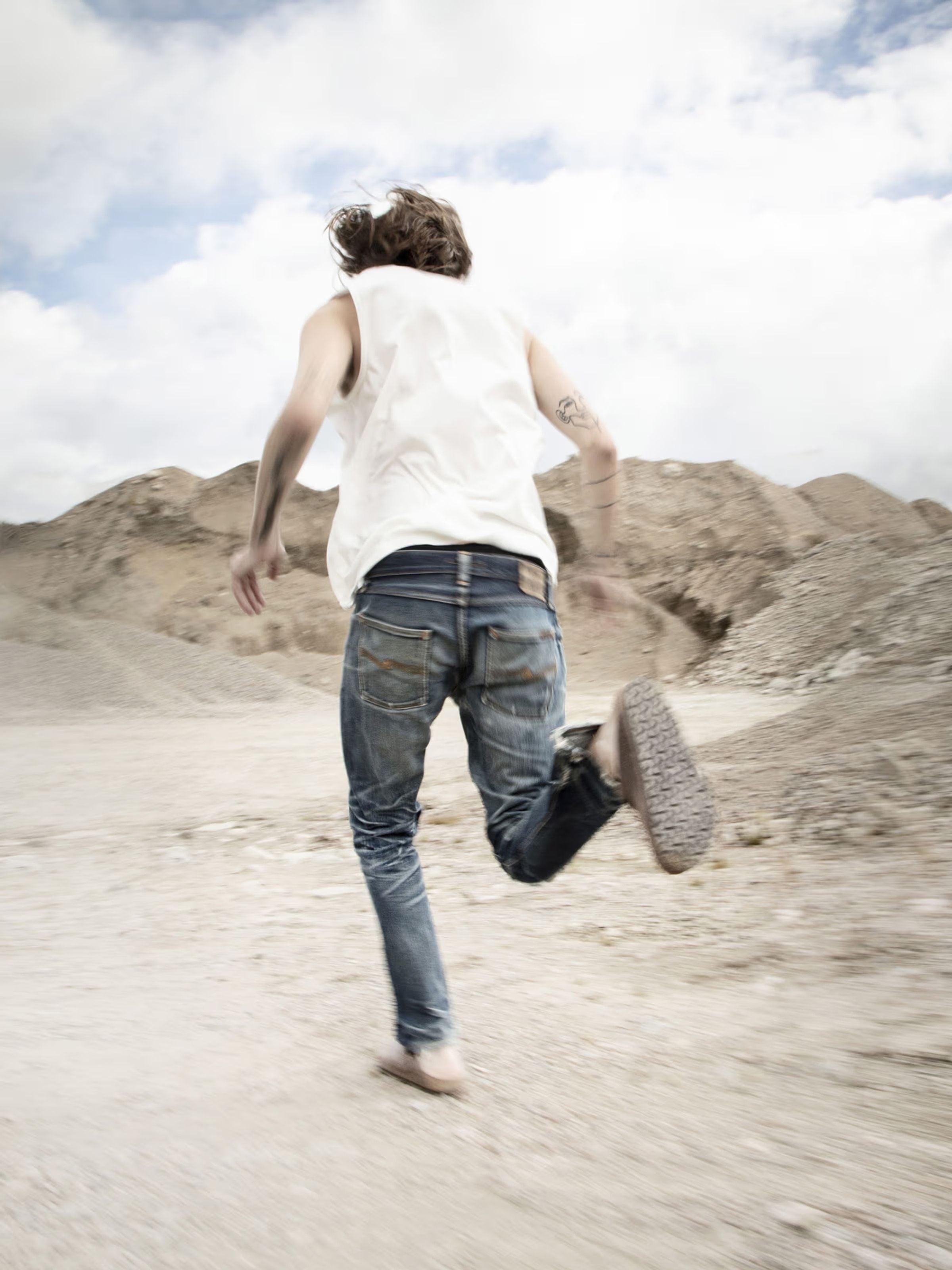 Nudie Jeans Gritty Jackson selvedge jeans in dry blue, shown running in an outdoor lifestyle setting.