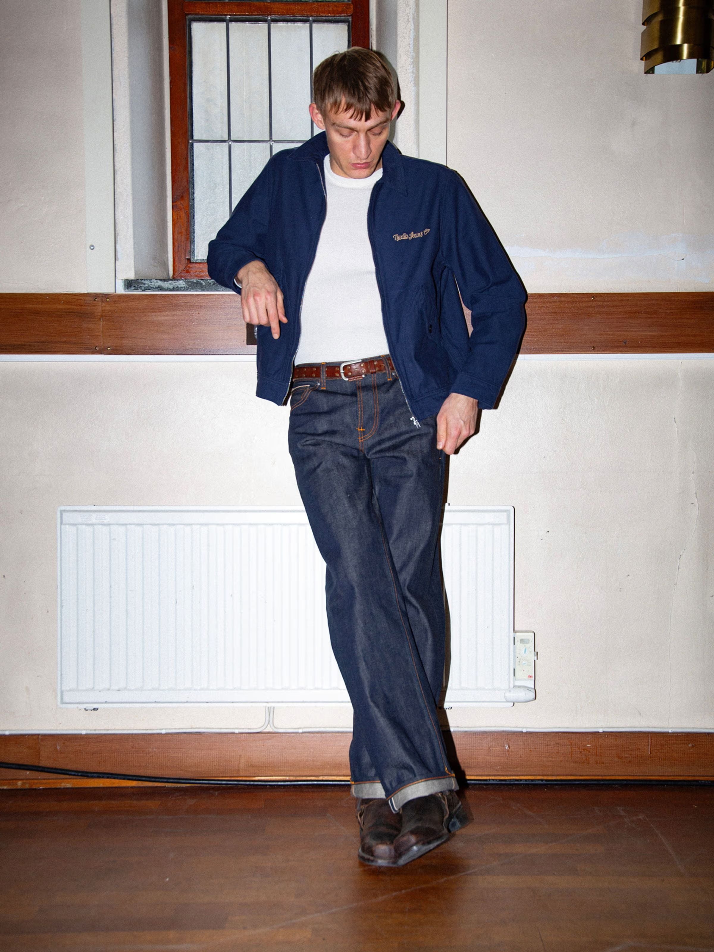 Nudie Jeans Tuff Tony Dry Selvedge, men's loose fit jeans in dark blue organic cotton selvedge denim worn with a jacket.