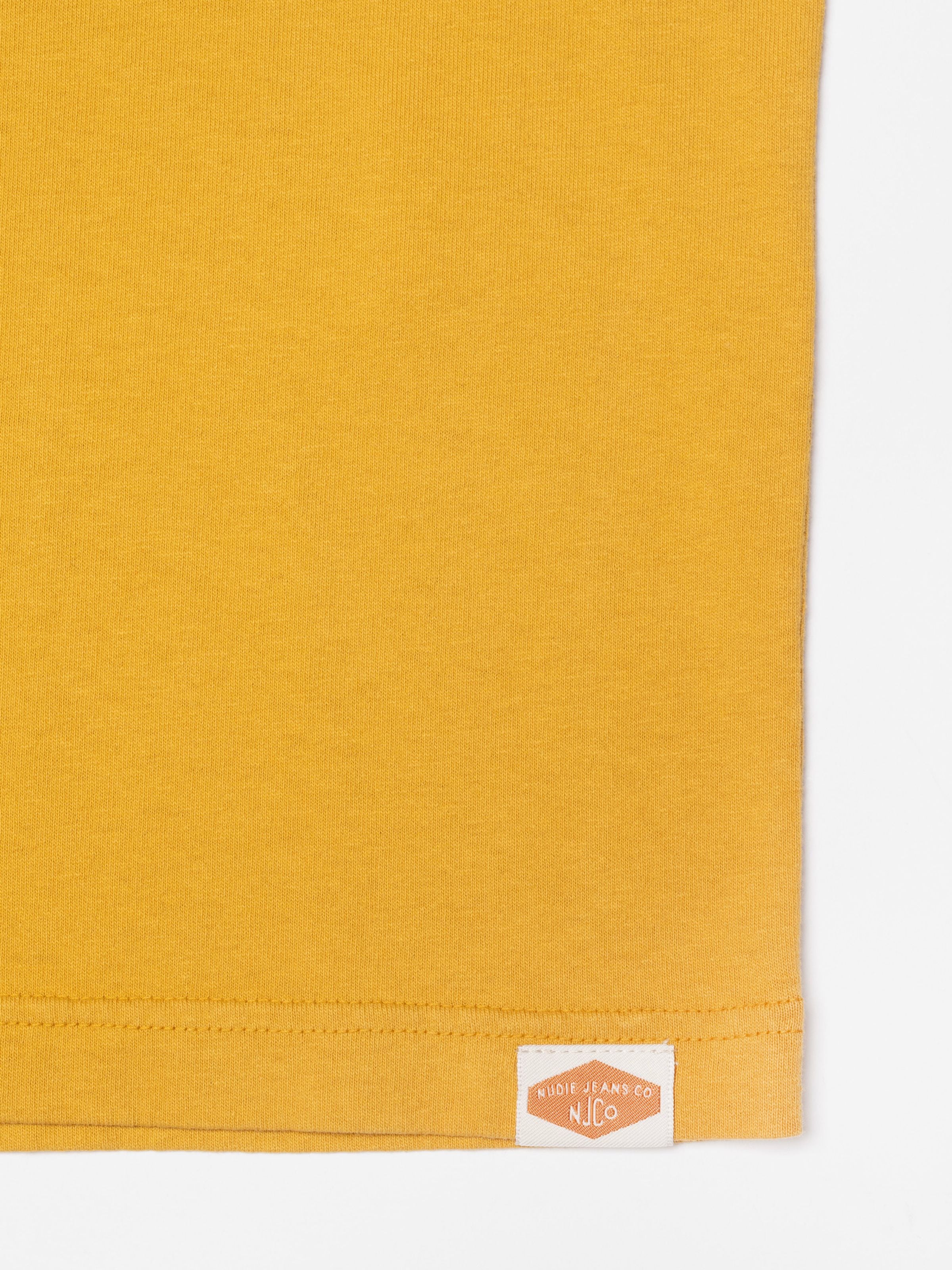 Nudie Jeans Uno Everyday T-Shirt in Old Yellow, showing the pigment-dyed organic cotton jersey texture and hem tag.