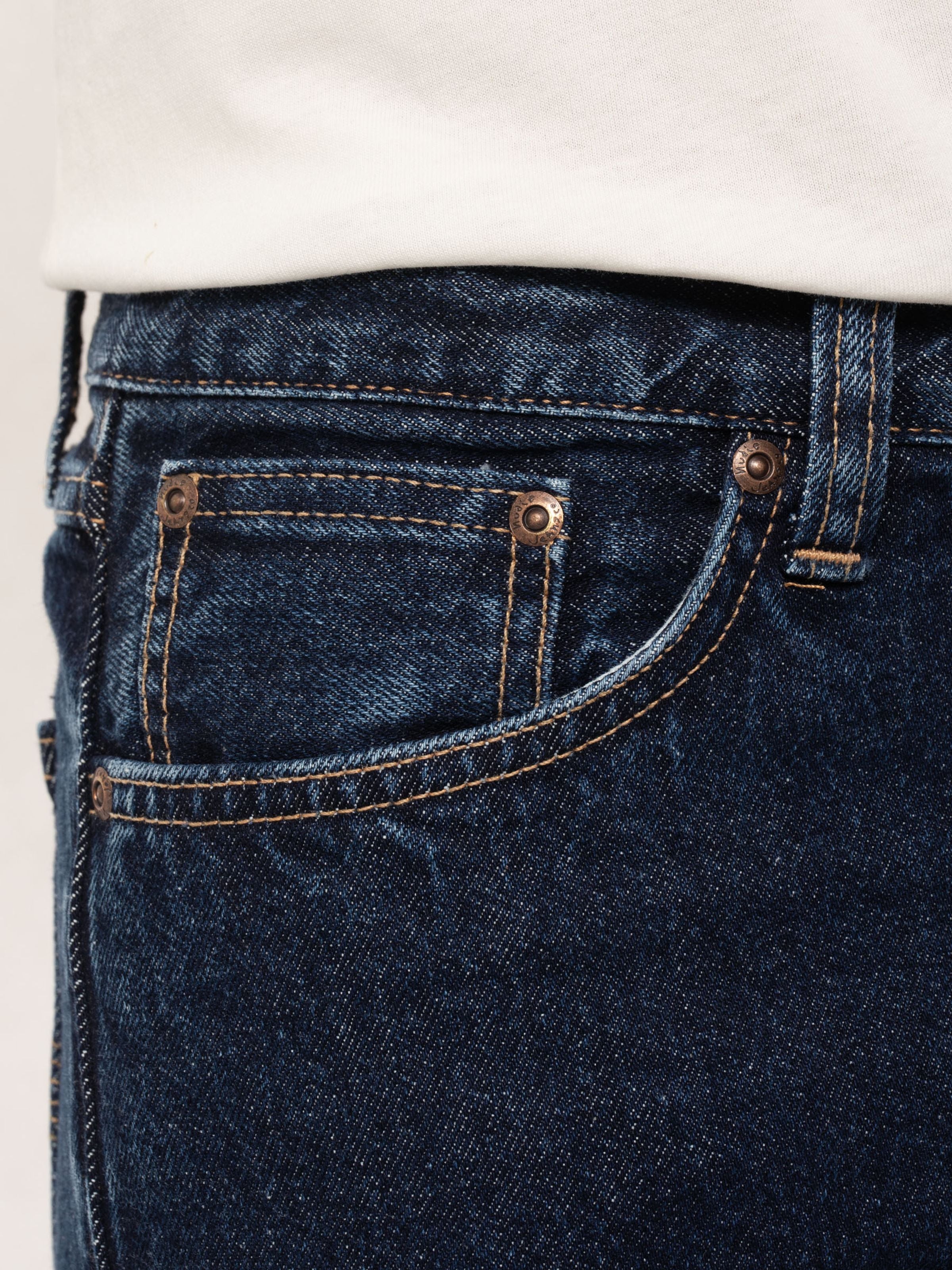 Nudie Jeans Steady Eddie II Heavy Rinse, Nahaufnahme der Vordertasche mit tabakfarbenen Nähten und Kupfernieten.