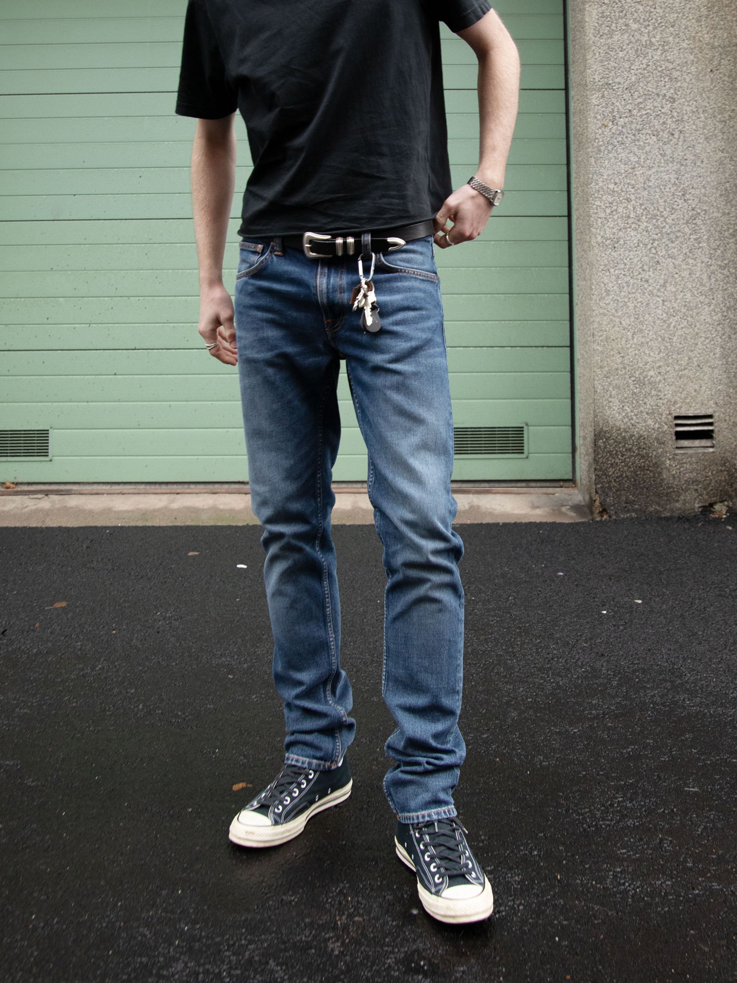 Nudie Jeans Lean Dean Troubled Sea, men's slim tapered stretch jeans in dark blue wash, worn outdoors in a lifestyle setting.
