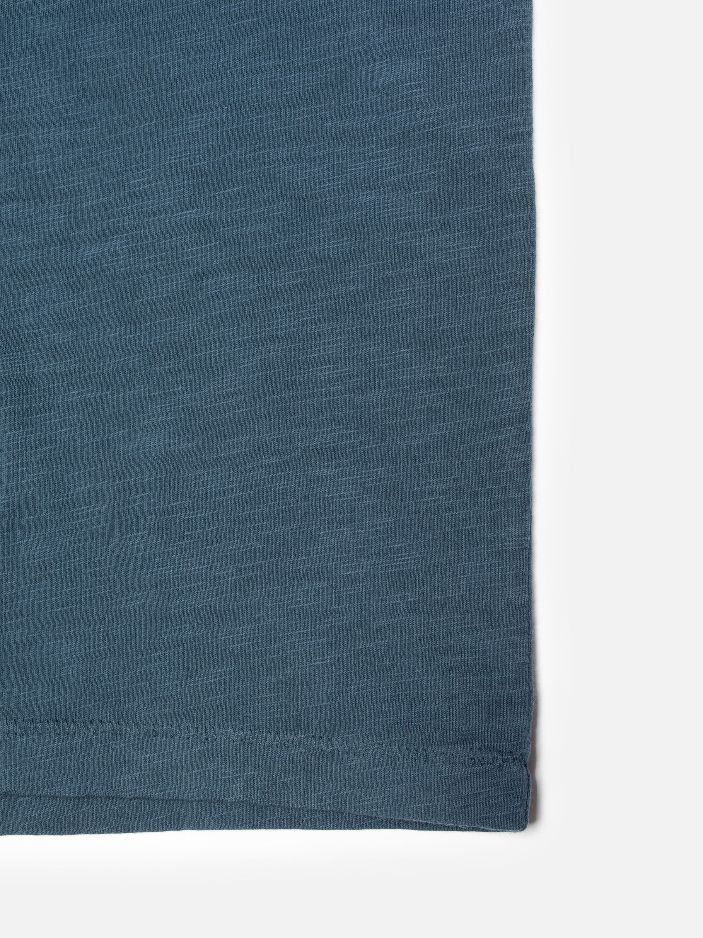 Nudie Jeans Roffe Slub T-Shirt in Blue, showing a close-up of the slubby fabric and mouse teeth stitching at the hem.