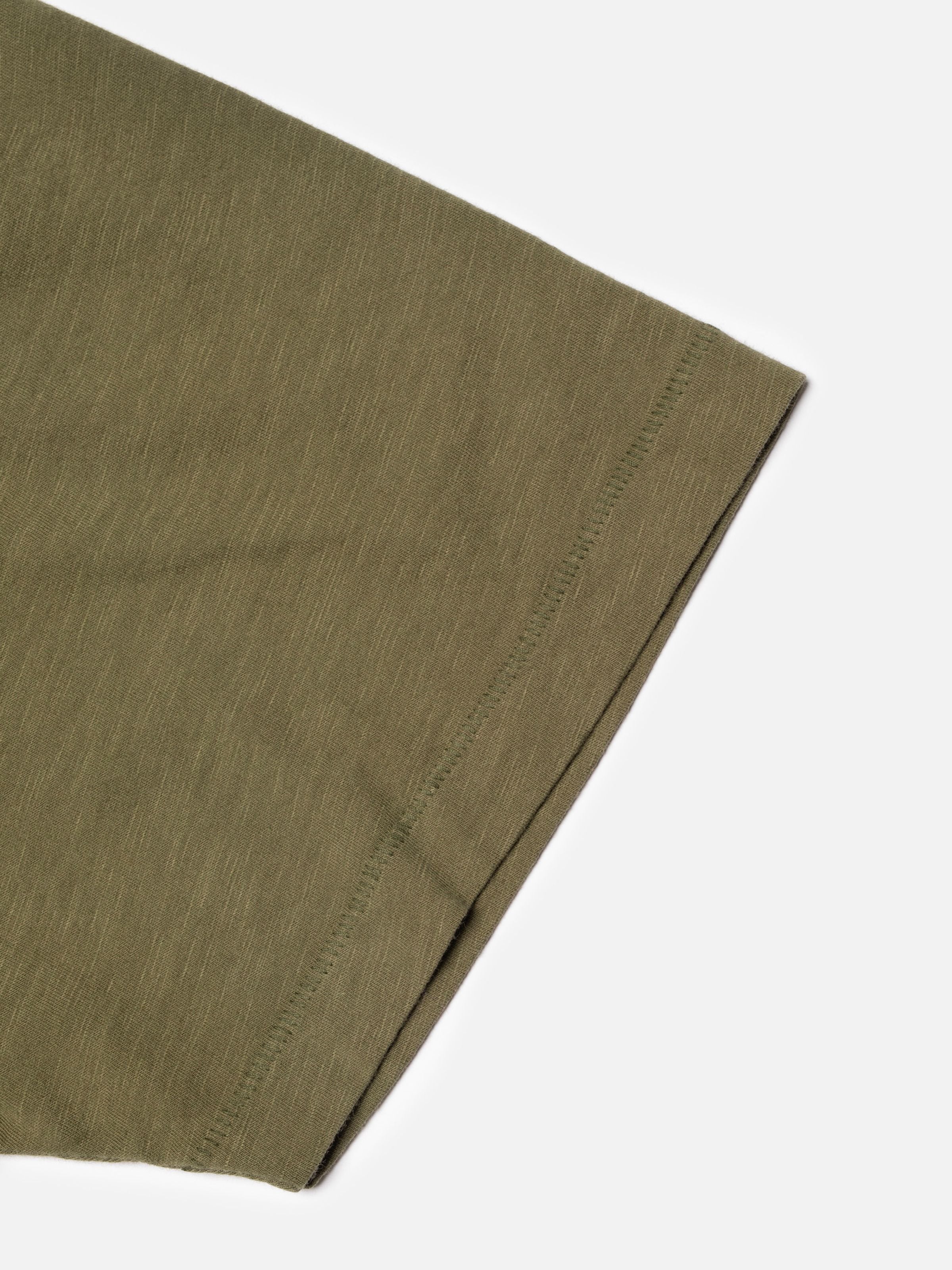 Nudie Jeans Roffe Slub T-Shirt in Olive Green, showing a close-up of the hem and organic slub cotton fabric texture.