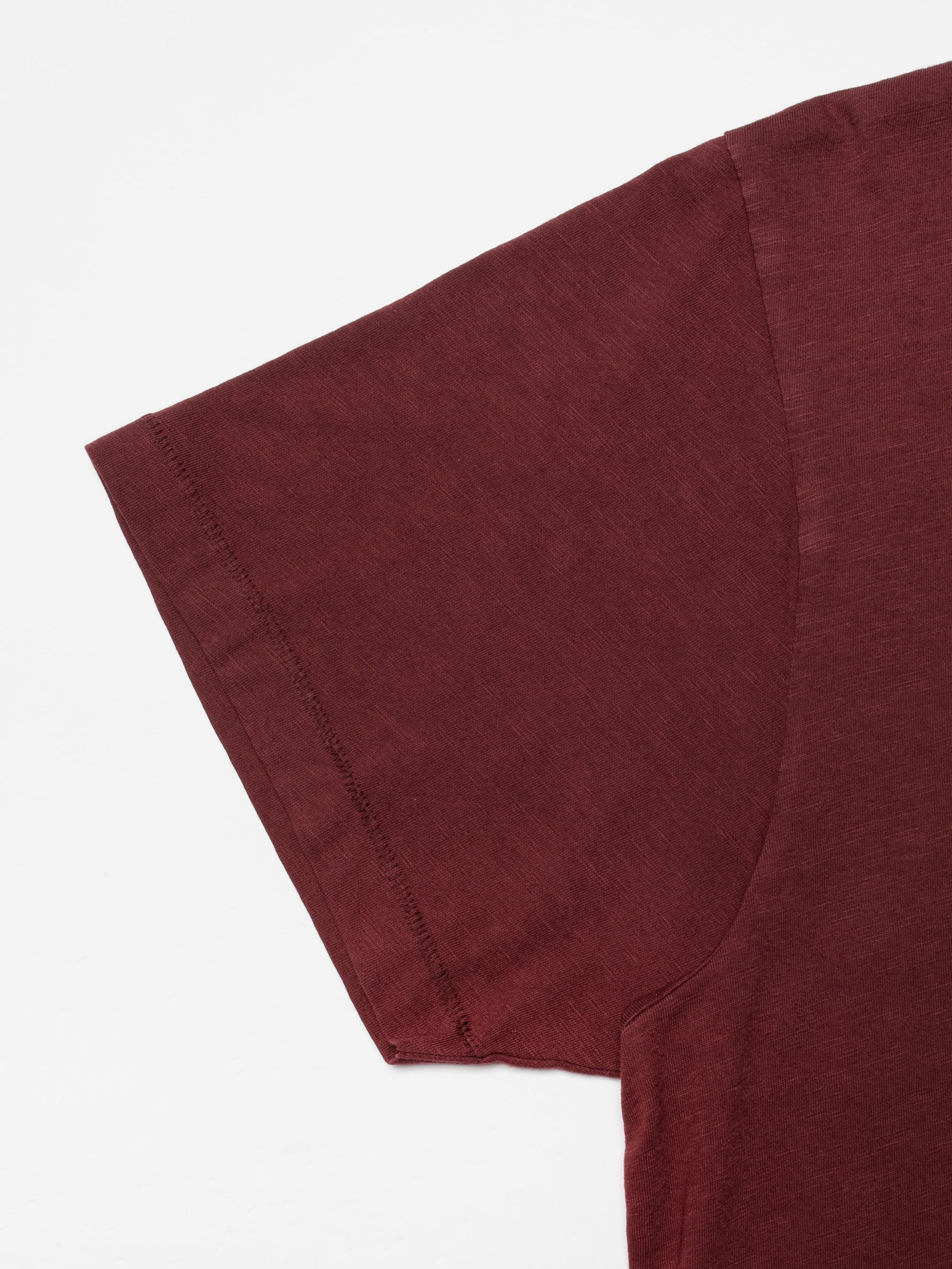Nudie Jeans Roffe Slub T-Shirt in Burgundy, a close-up of the organic cotton fabric texture and sleeve hem stitching.