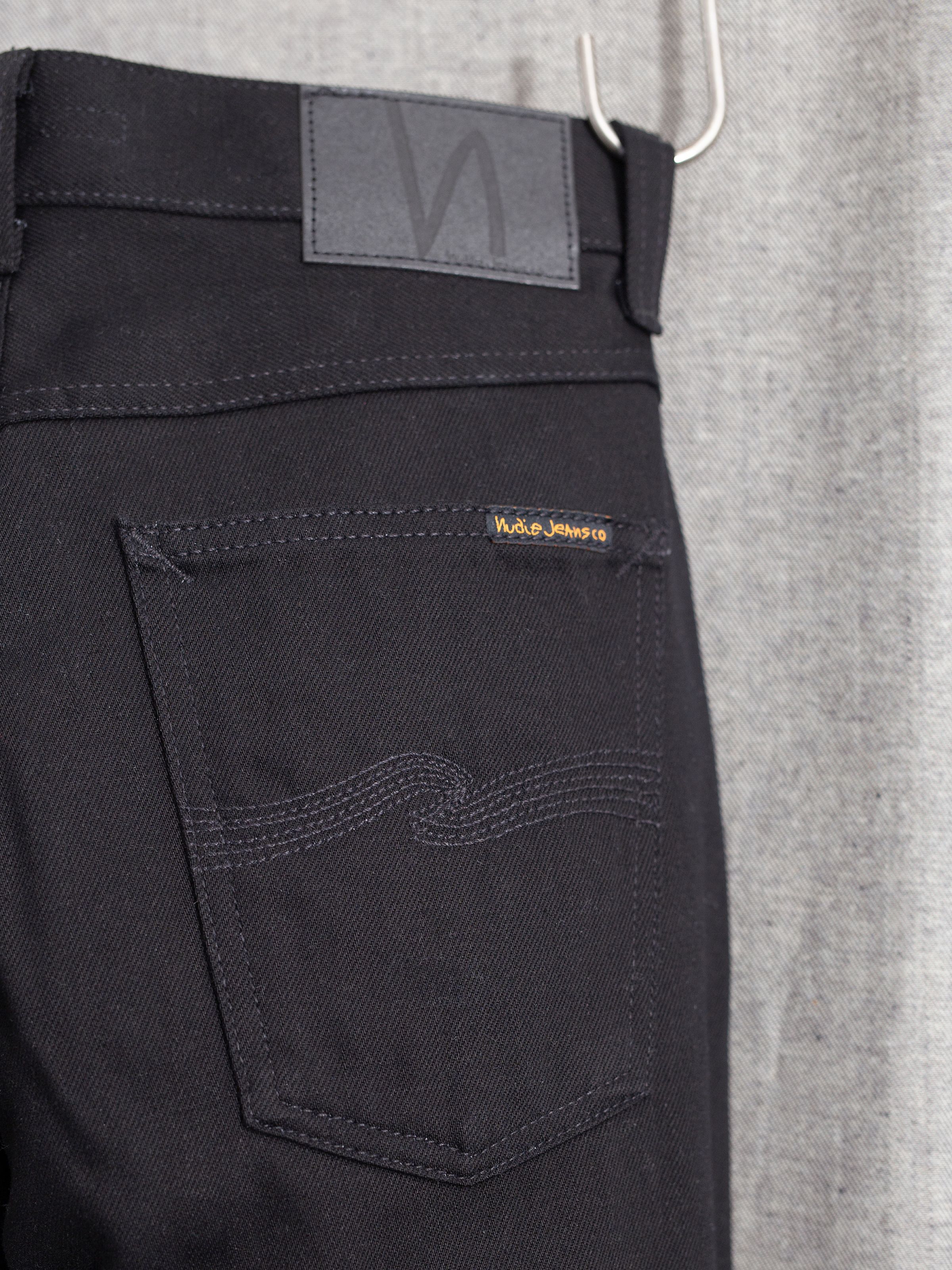 Nudie Jeans Gritty Jackson Dry Everblack, men's regular fit jeans, showing a close-up of the back pocket and jacron patch.
