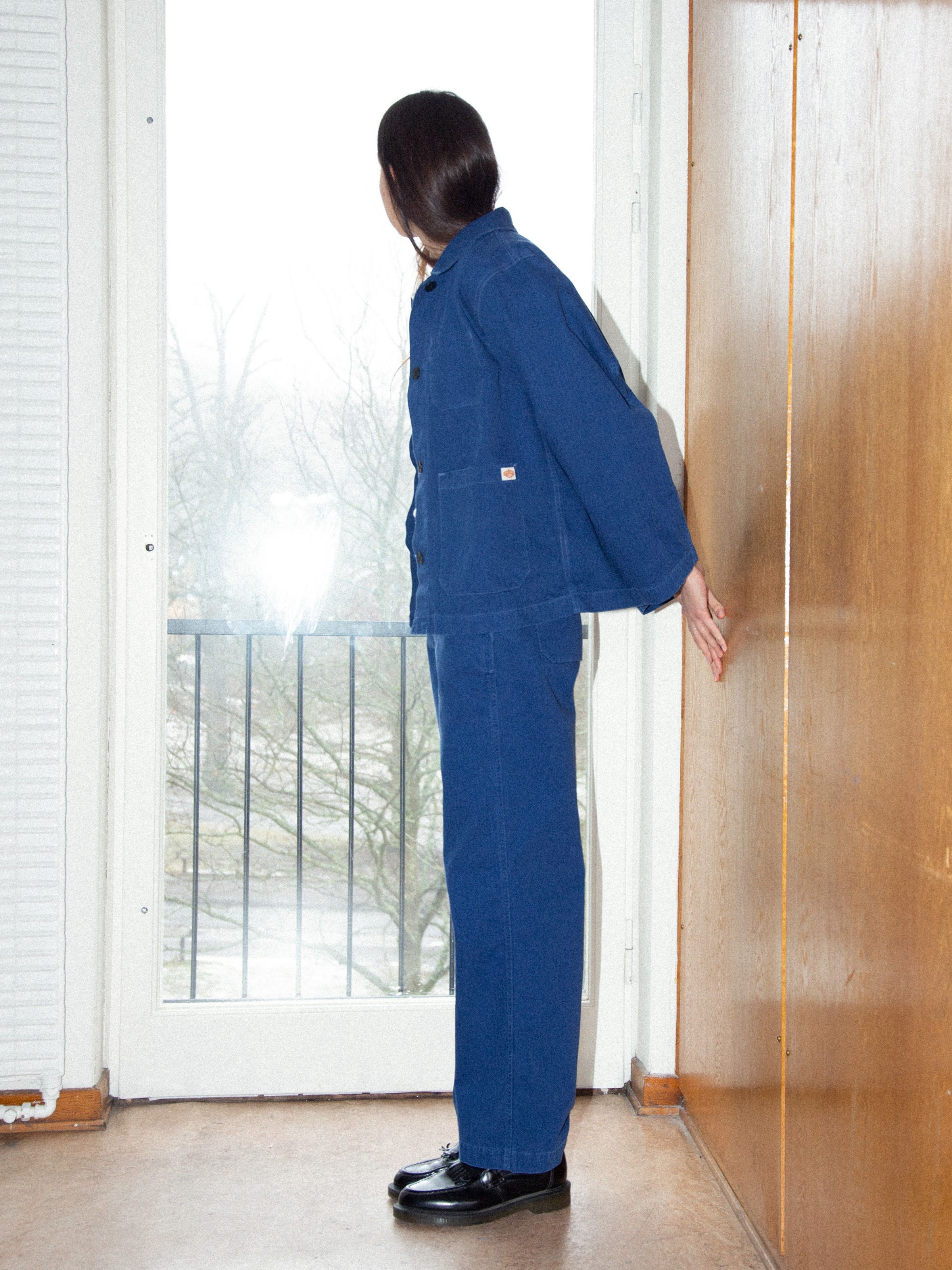 Nudie Jeans Wendy Herringbone Pants in Blue, shown as a matching workwear set on a model standing by a window.