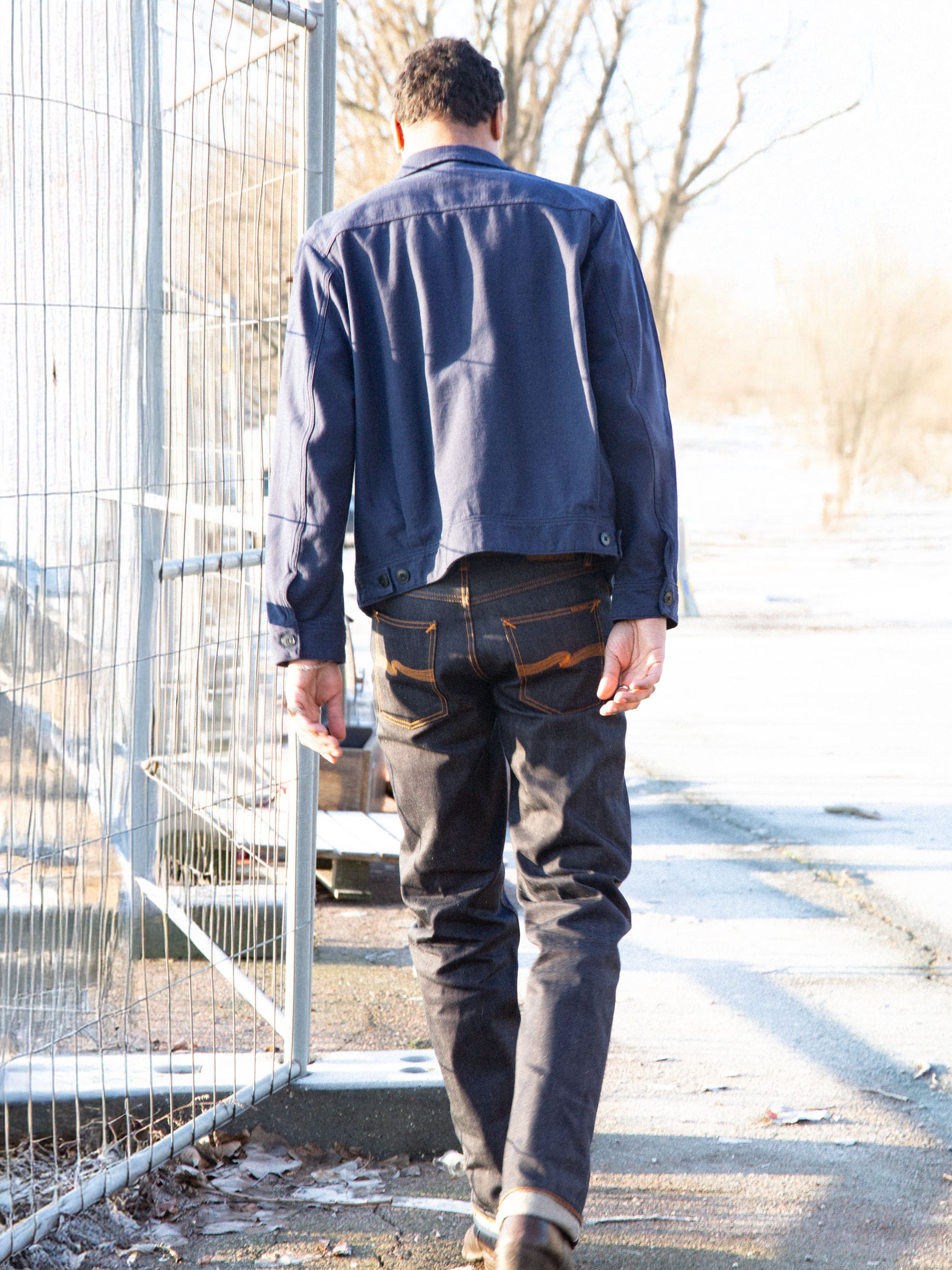 Nudie Jeans Rad Rufus Dry Selvage, men's regular fit straight leg jeans shown from the back on a model walking outdoors.