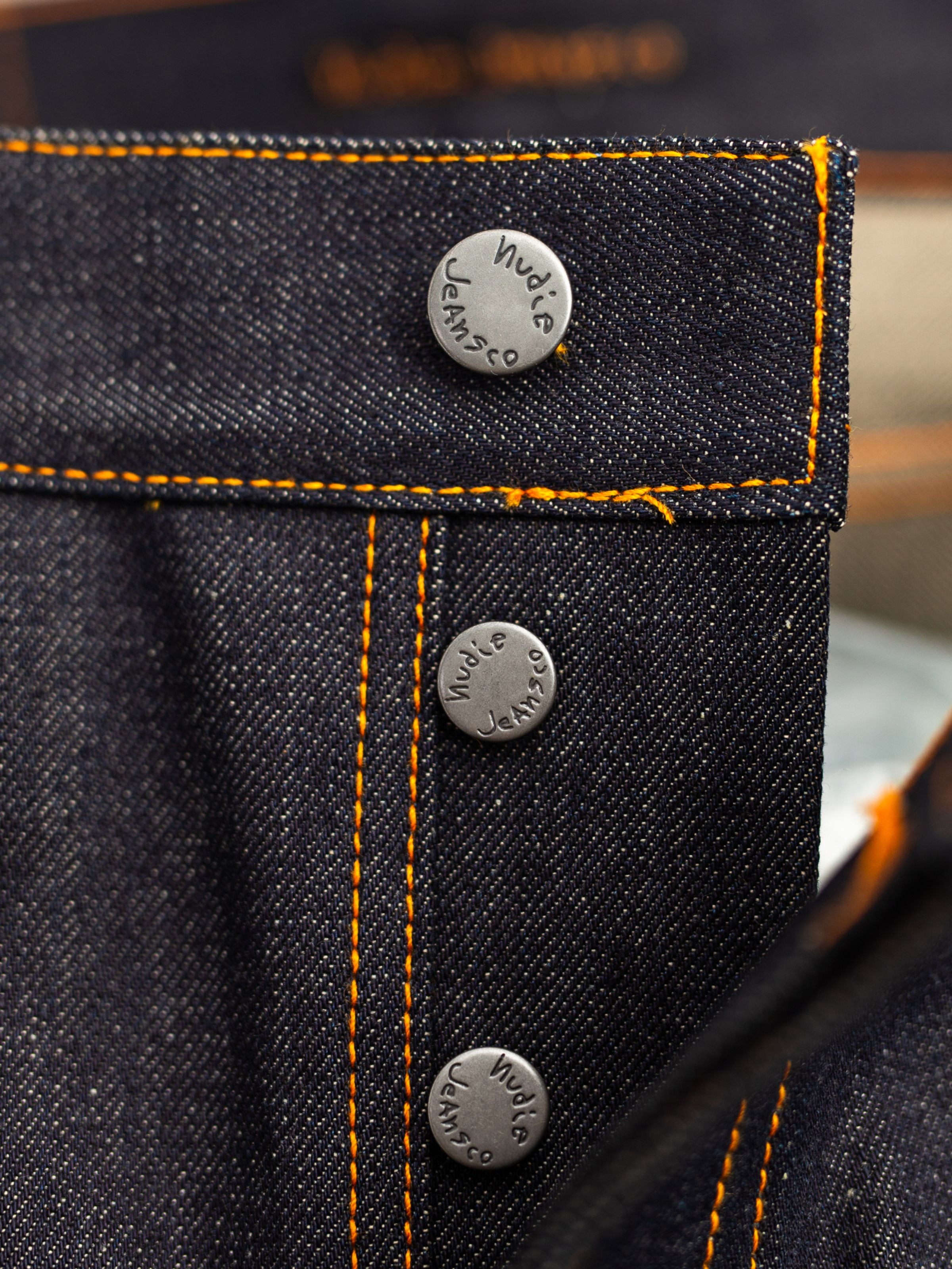 Nudie Jeans Rad Rufus Dry Selvage, close-up of antique silver button fly and orange stitching on dry selvedge denim.