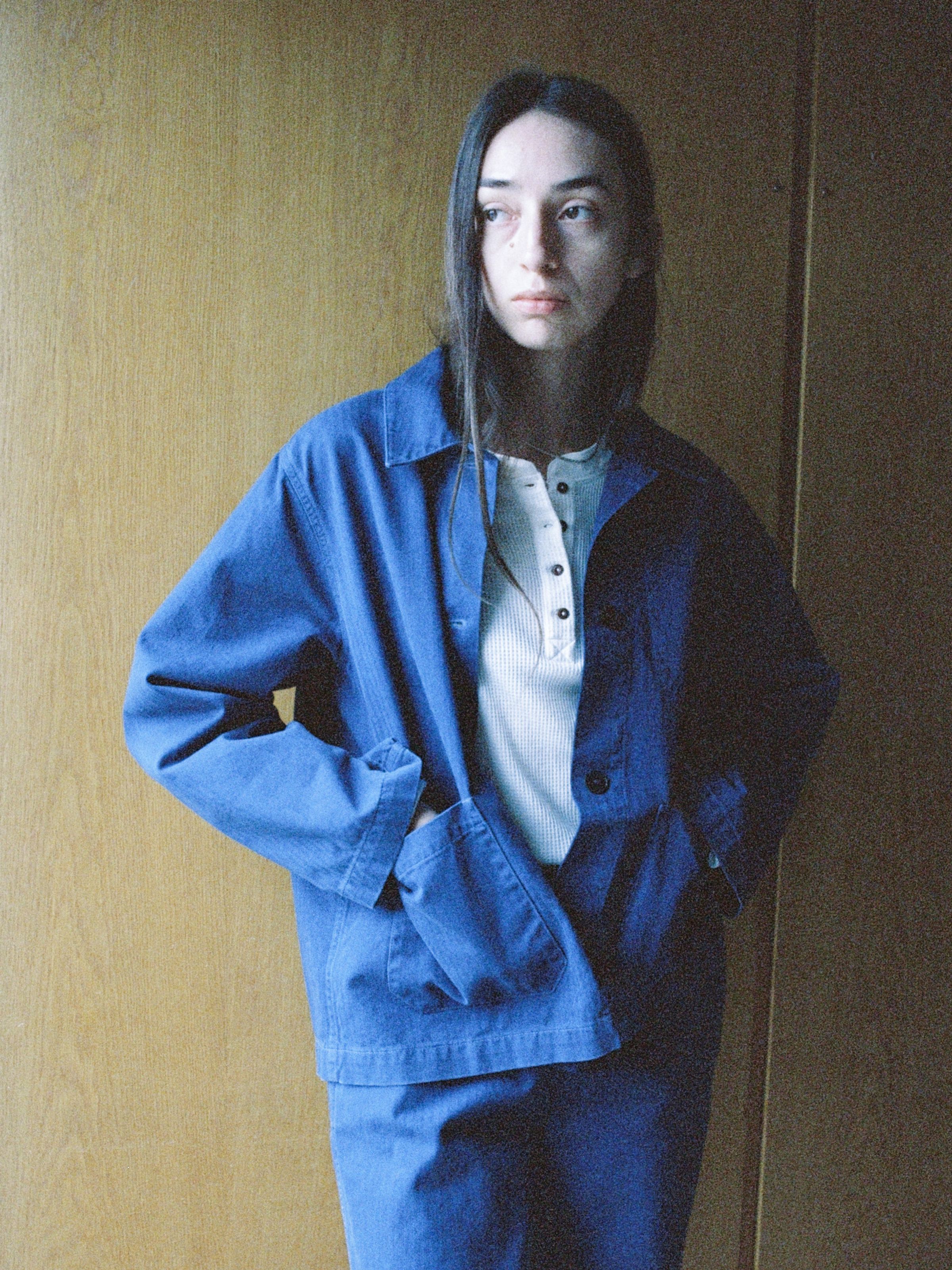 Nudie Jeans Lovis Herringbone Jacket Blue, a women's regular-fit work jacket shown on a model against a wood backdrop.