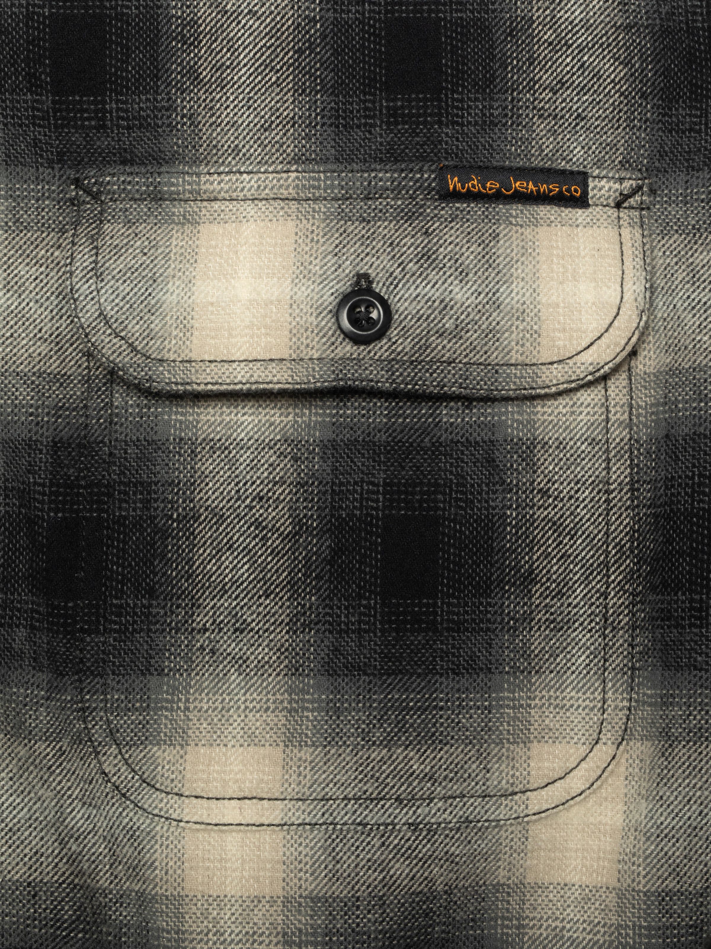 Nudie Jeans Glenn Padded Shadow Check Shirt Black, a men's flannel overshirt, shown in a close-up of the chest pocket.