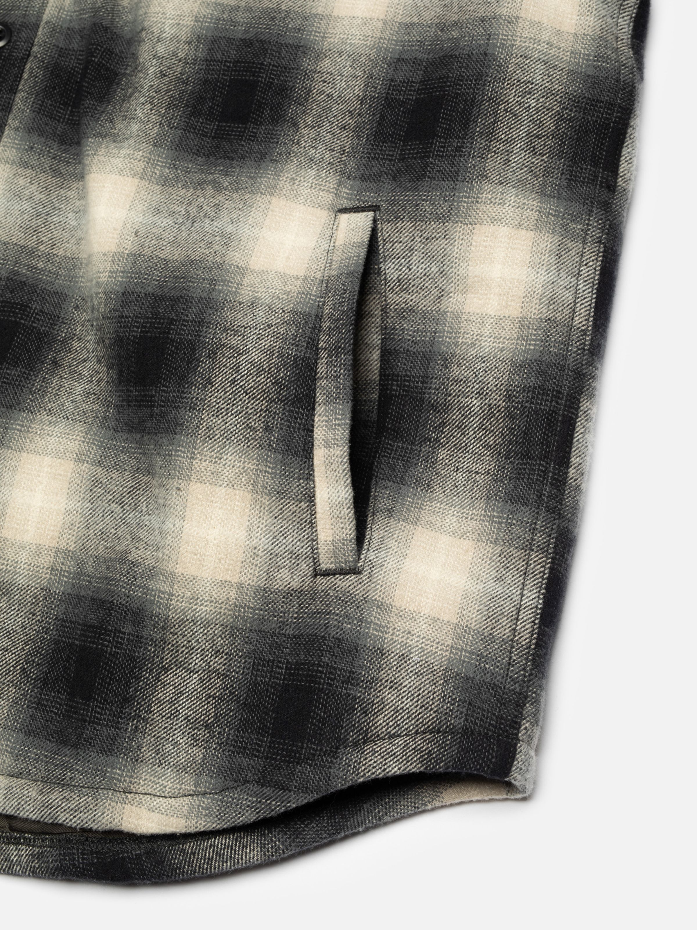 Nudie Jeans Glenn Padded Shadow Check Shirt Black, a men's flannel overshirt, shown in a close-up detail of the side pocket.