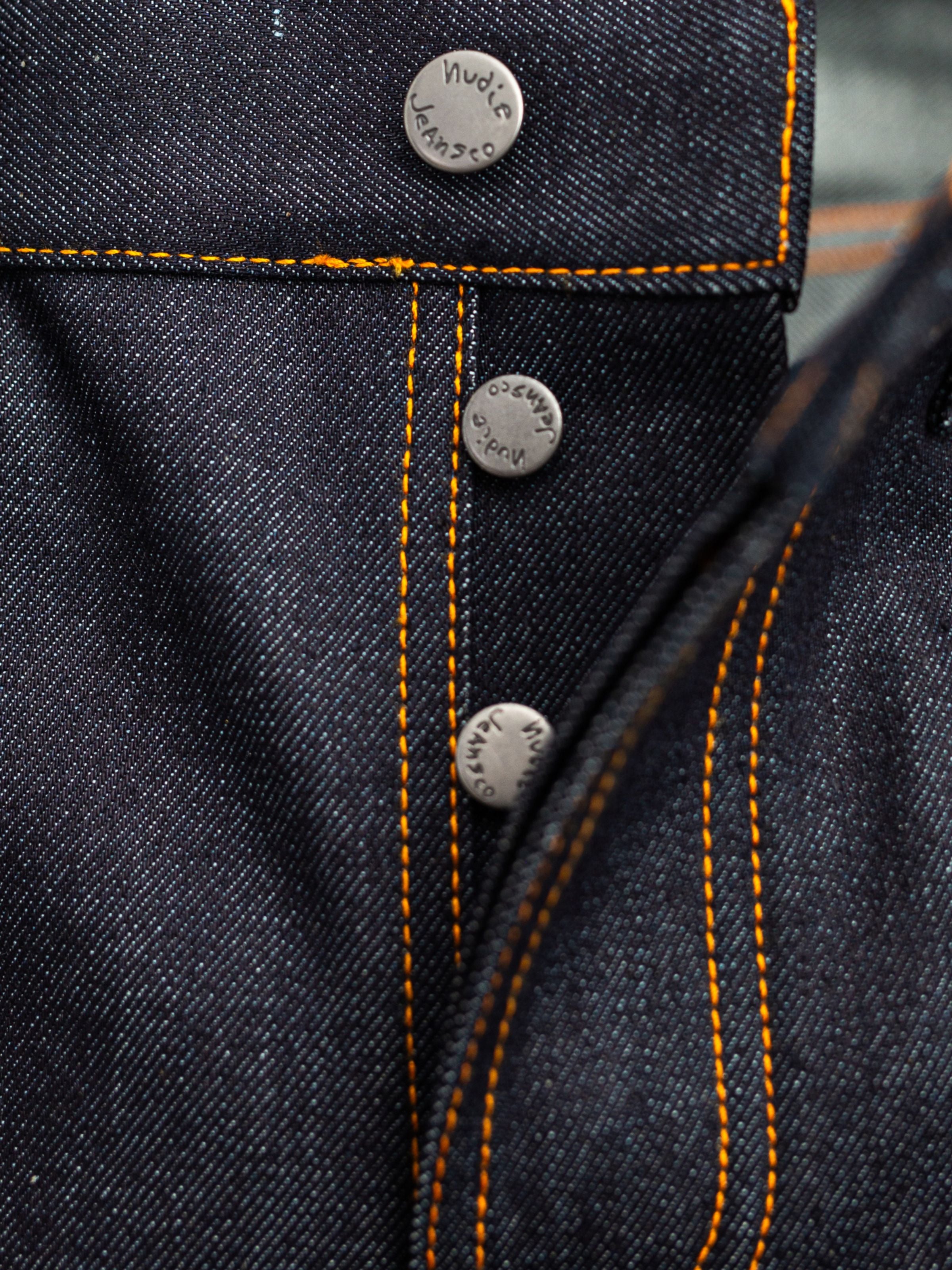 Nudie Jeans Solid Ollie Dry Japan Selvedge, close-up of the button fly and orange contrast stitching on dark denim.
