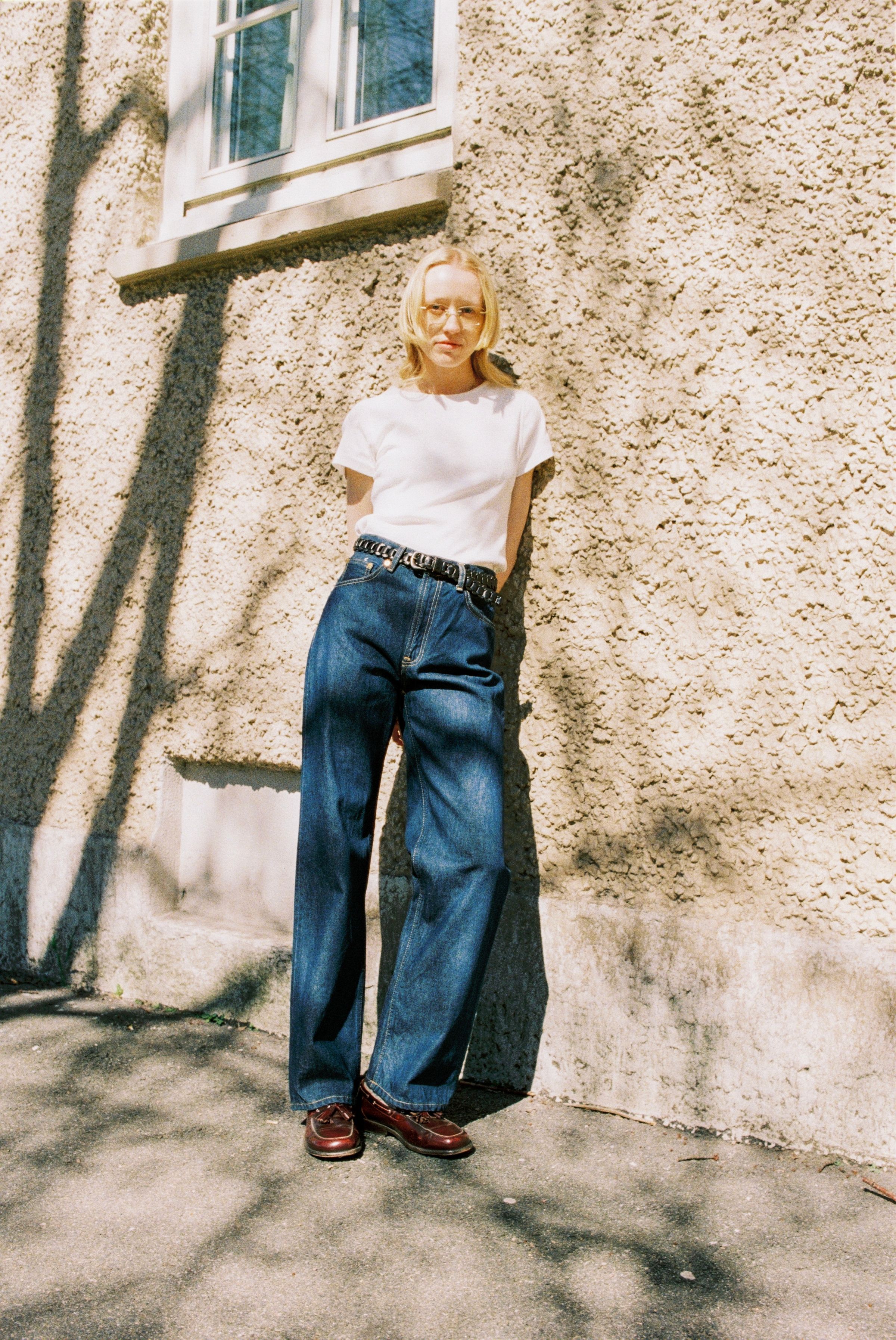 Nudie Jeans Clean Eileen Classic Blue, loose wide-leg jeans in organic cotton, shown on a model leaning against a wall.
