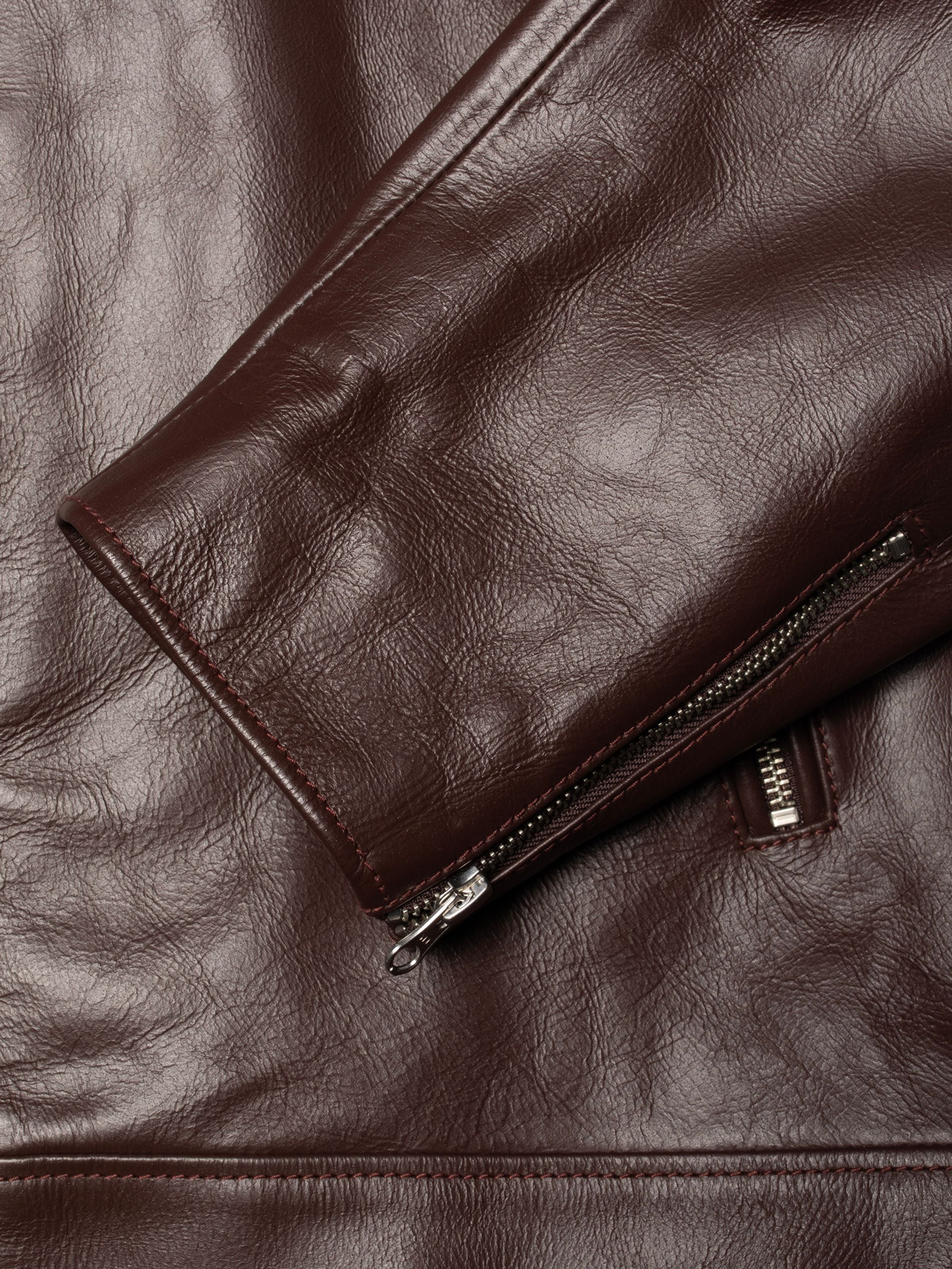 Nudie Jeans Eddy Rider Leather Jacket in Bordeauxrot, Nahaufnahme von Büffelleder und silbernem Ärmel-Reißverschluss.