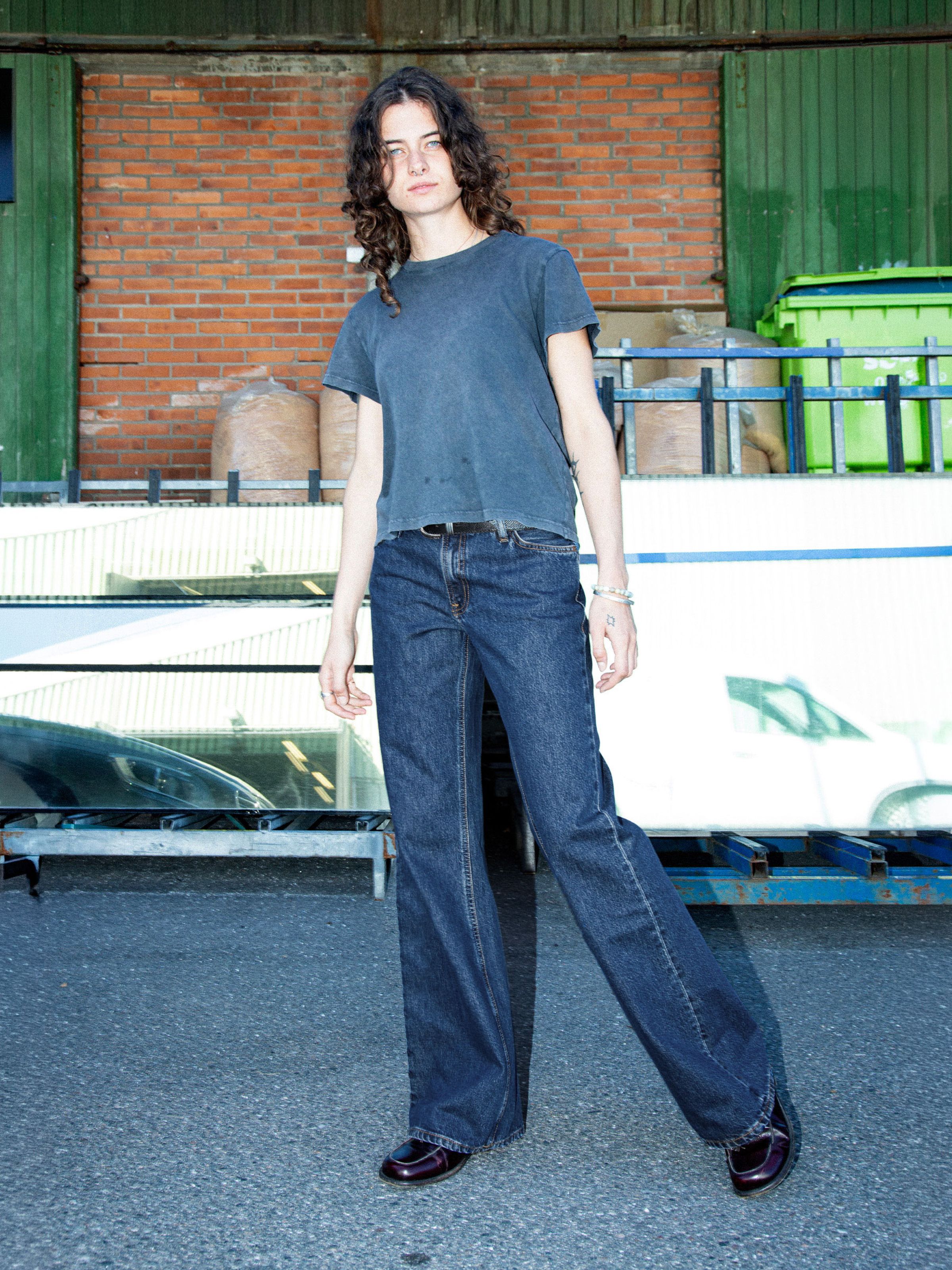 Nudie Jeans Wide Heidi Evening Jazz, Damenjeans in lockerer Passform, dunkelblaue Stonewash, Lifestyle-Aufnahme im Freien.