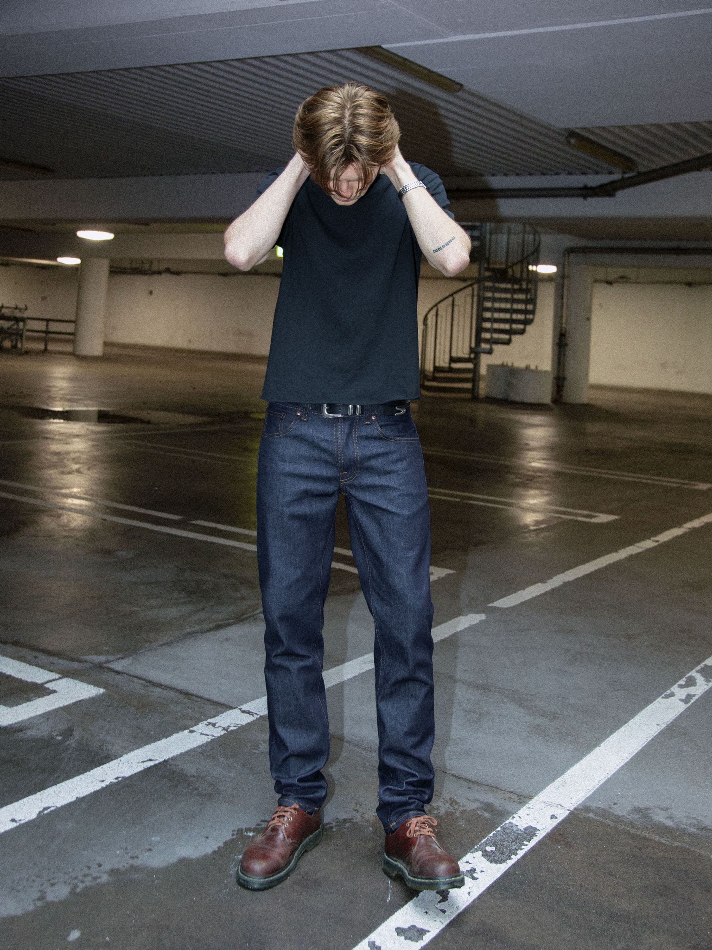 Nudie Jeans Solid Ollie Dry Abyss, slim straight jeans in blue organic cotton denim, worn in a parking garage.