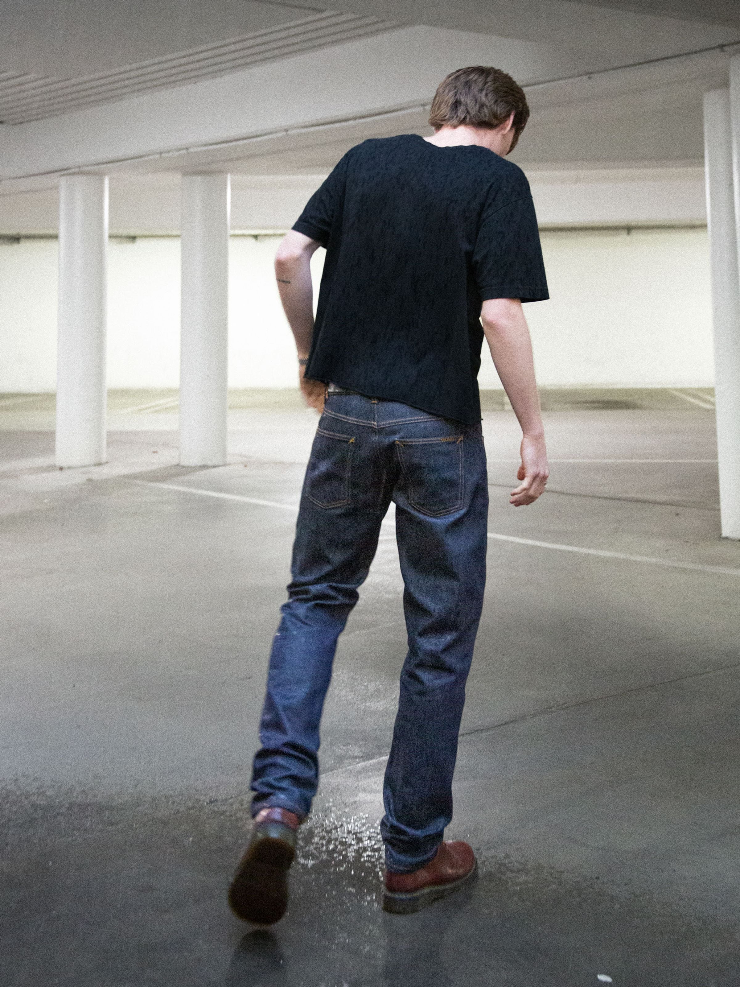 Nudie Jeans Solid Ollie Dry Abyss, schmale Herrenjeans, gezeigt in einer Lifestyle-Aufnahme von hinten in Dry Stretch Denim.
