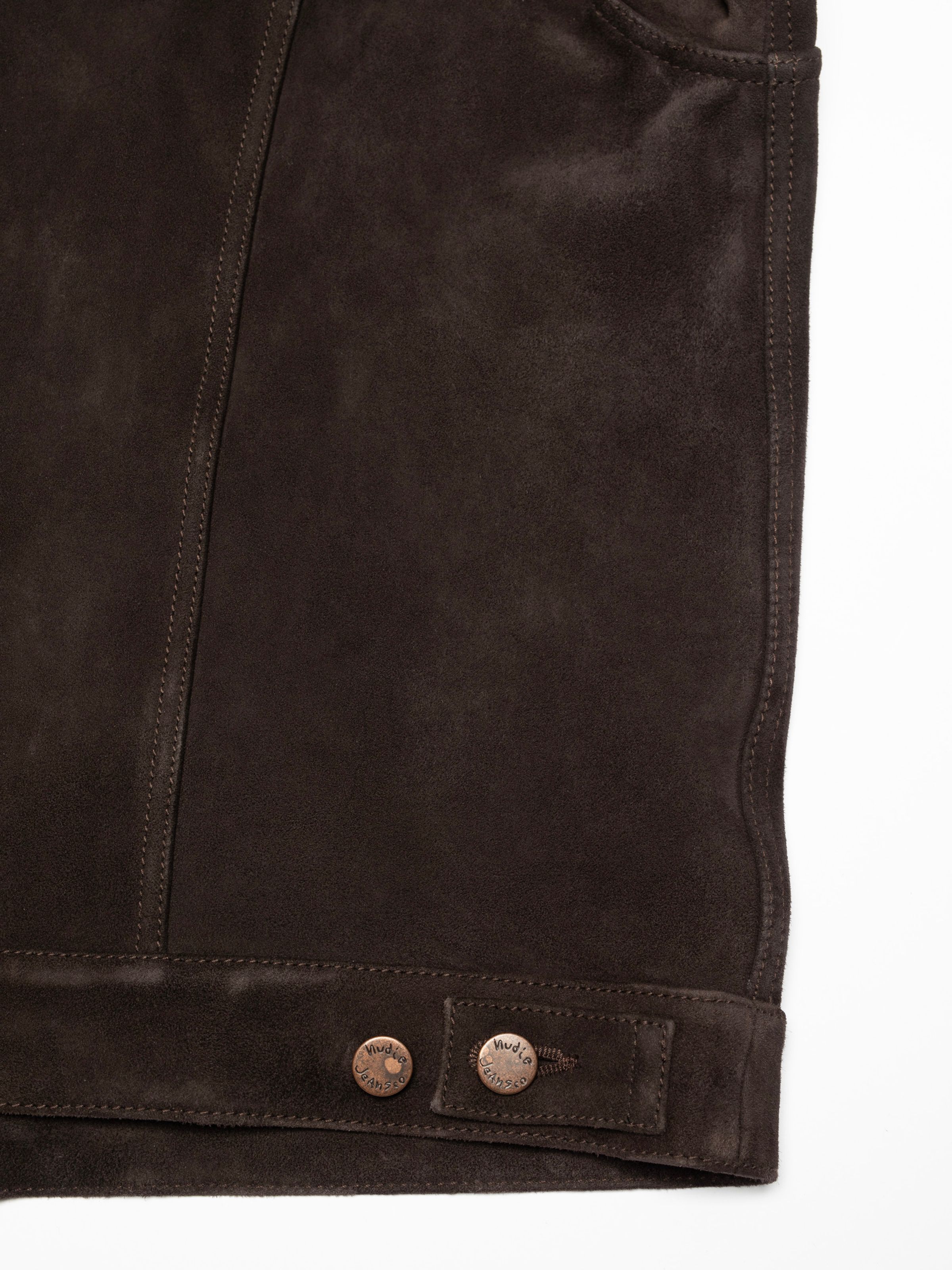 Nudie Jeans Dante II Suede Jacket in Dark Brown, a close-up showing the side hem, seams, and copper logo buttons.