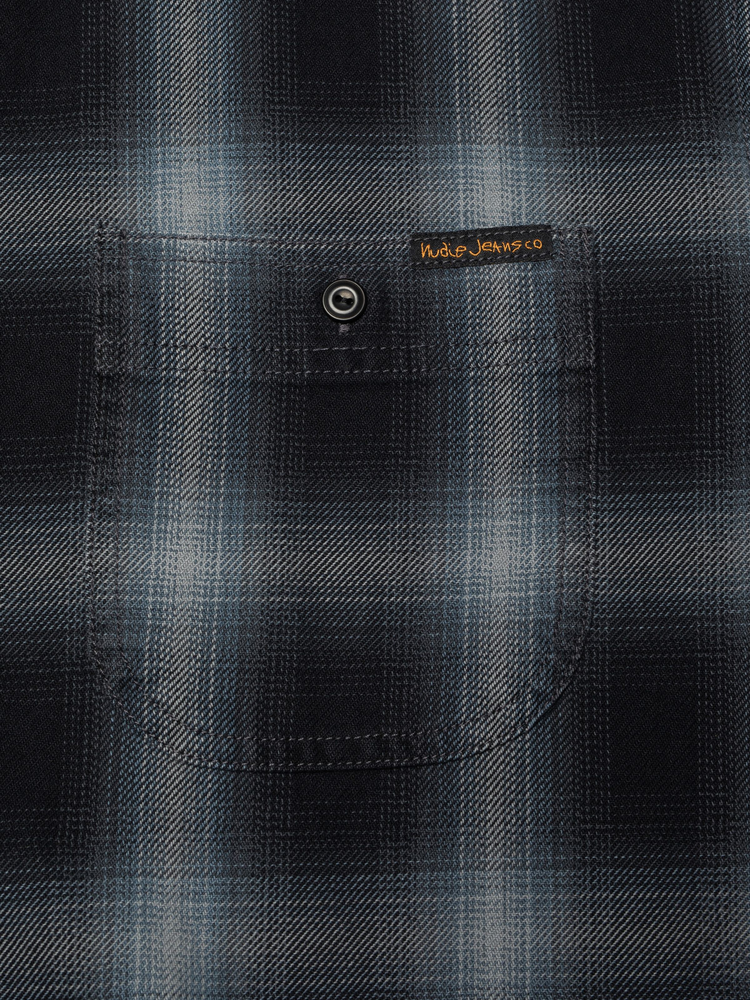 Nudie Jeans Julian Worker shirt, close-up of the shadow check chest pocket with its black button and Nudie Jeans logo label.