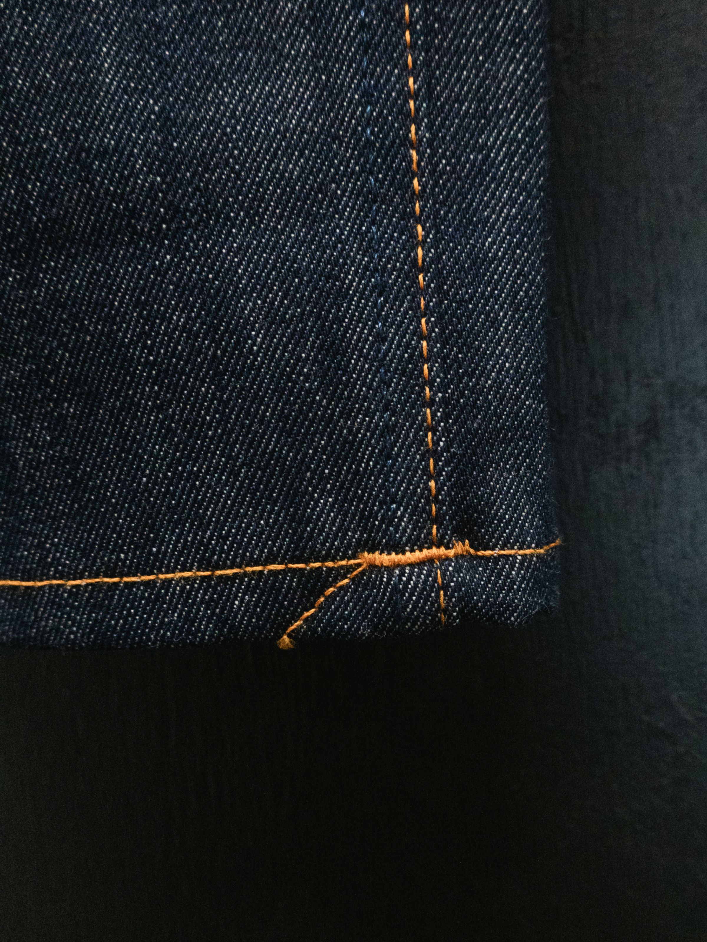 Nudie Jeans Tuff Tony Dry Sunburns, a men's loose fit jean in dry blue denim, shown in a close-up of the hem stitching.