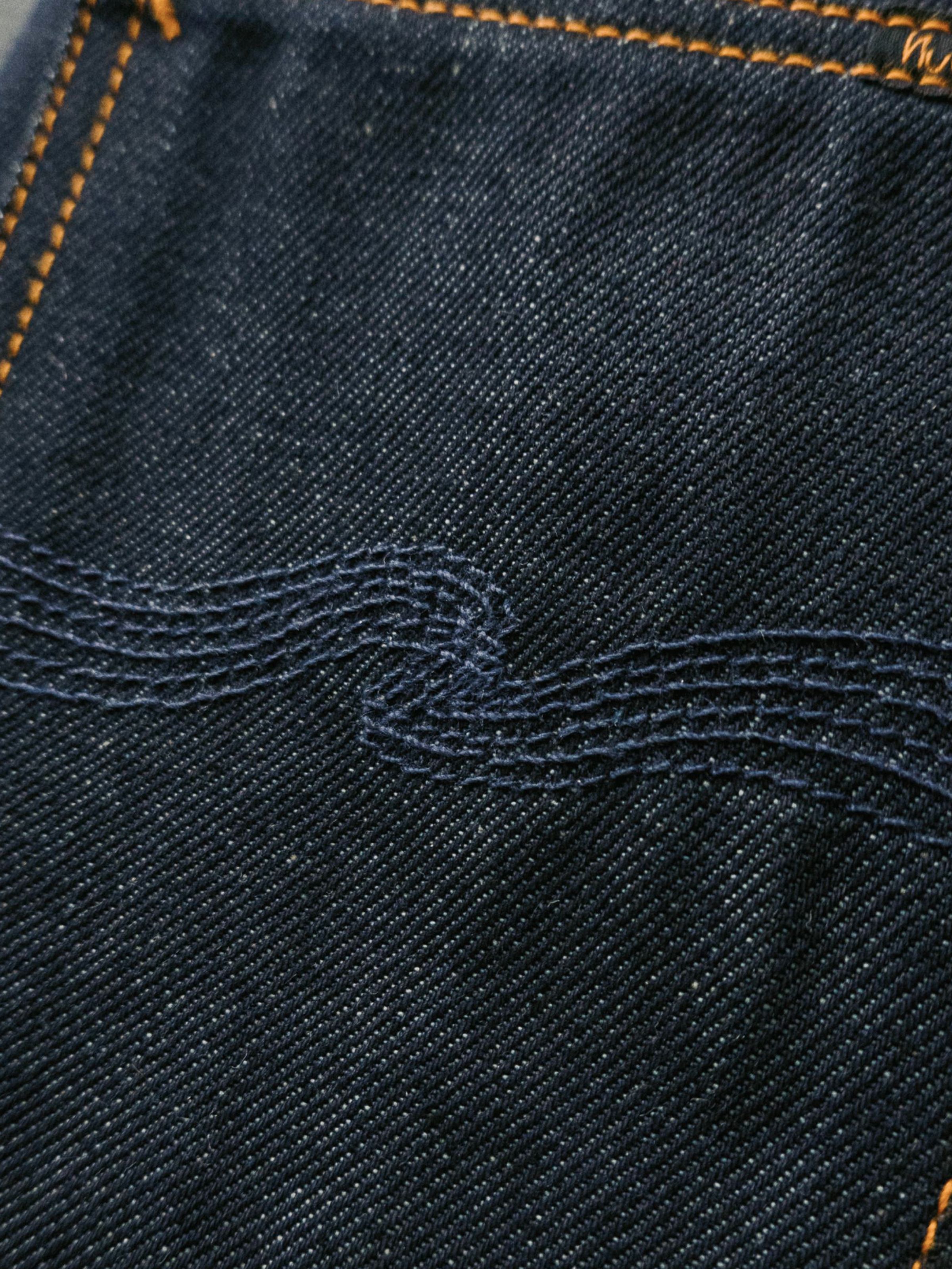 Nudie Jeans Rad Rufus Dry Dusk Selvage, men's regular fit jeans, showing a close-up of the back pocket embroidery.