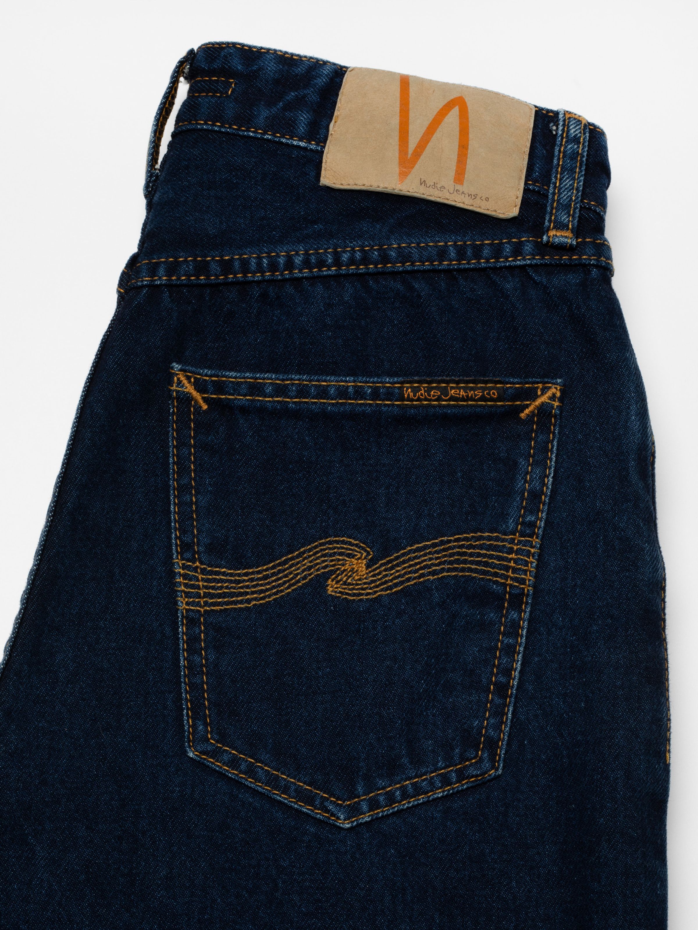 Nudie Jeans Lofty Lo in Indigo Dipped, Nahaufnahme der Gesäßtasche mit tabakfarbenen Nähten und Patch am Bund.