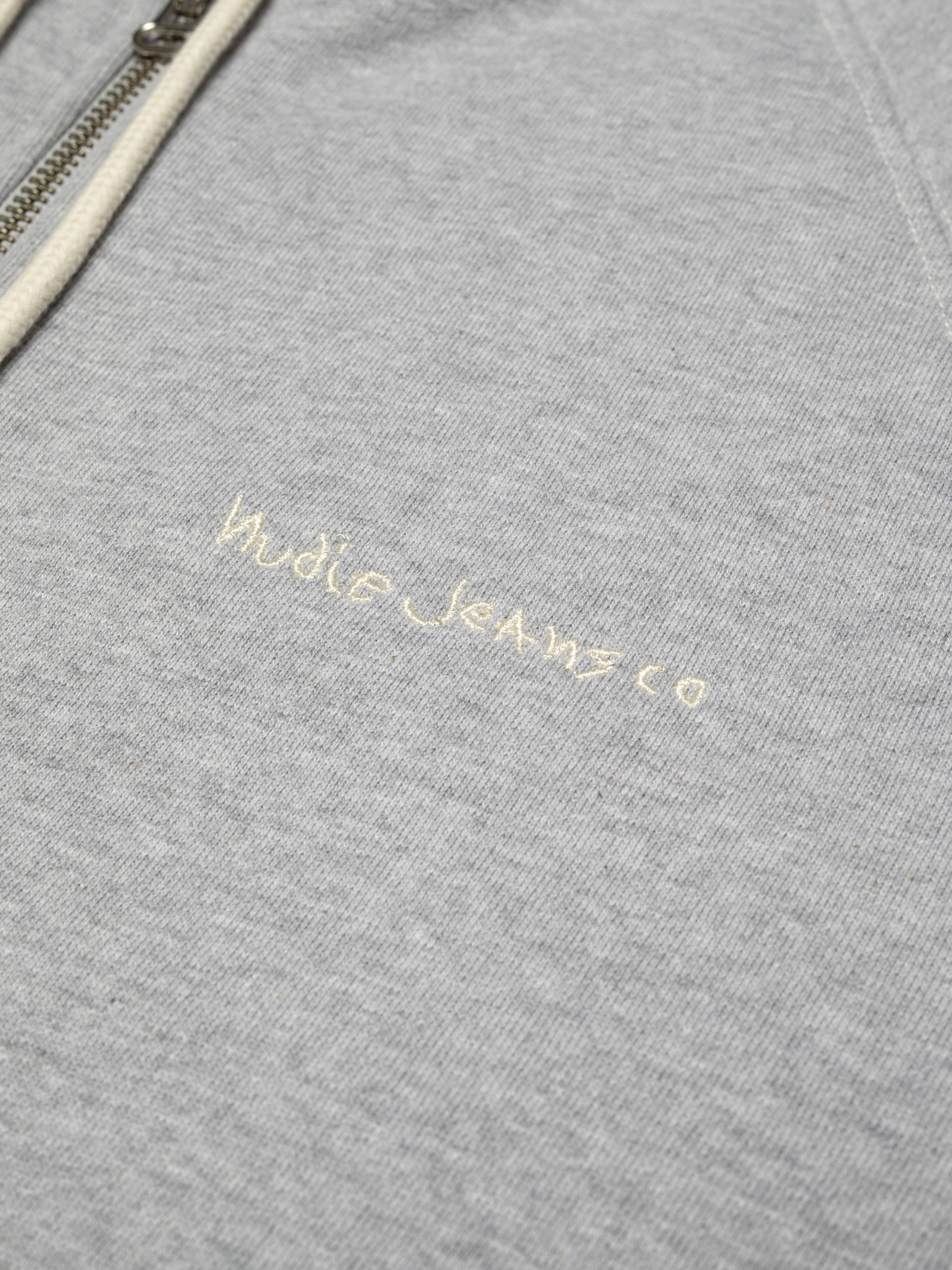 Nudie Jeans Gunde Logo Zip Hoodie in Greymelange, a close-up view of the embroidered logo on the chest.