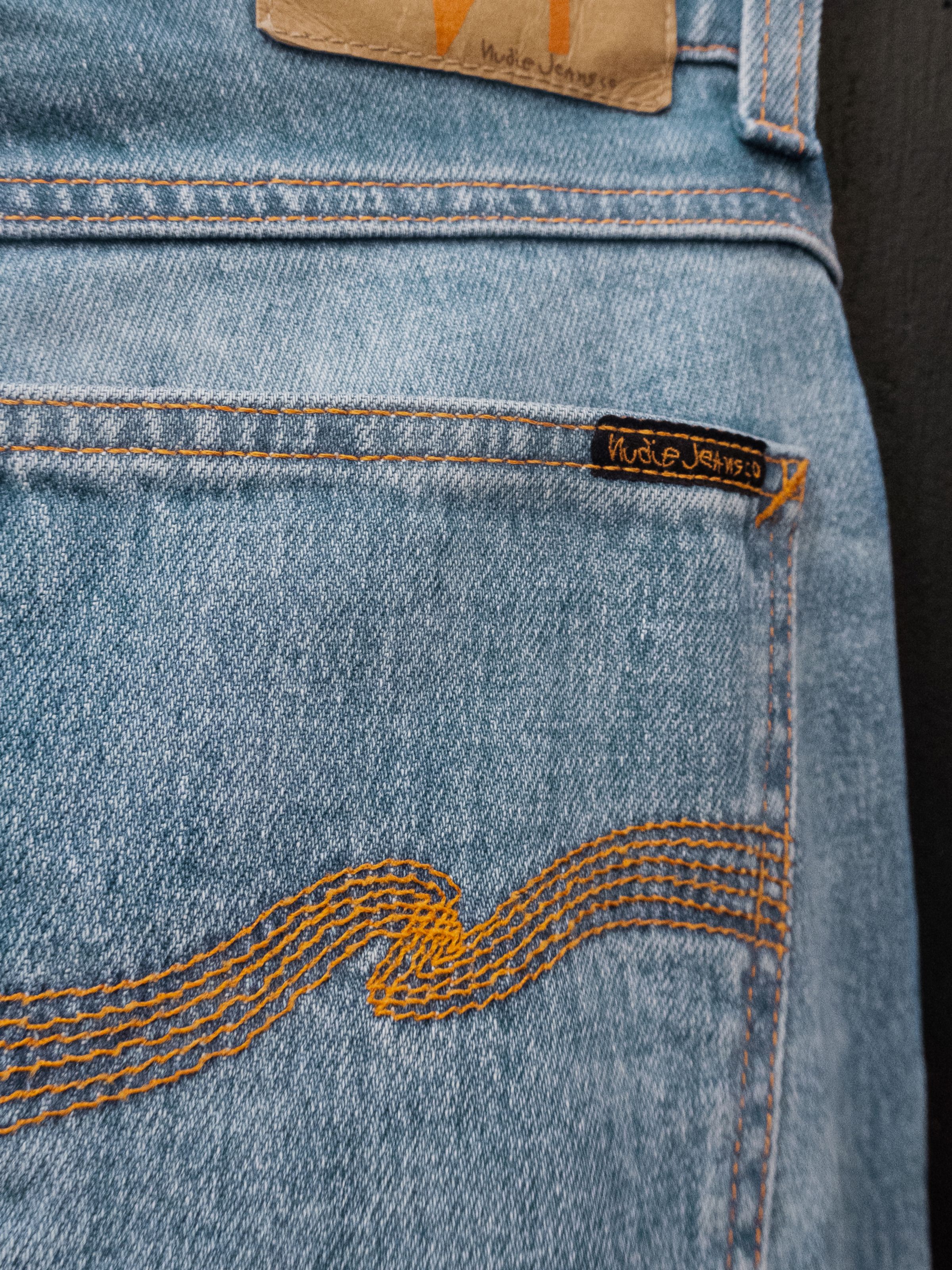 Nudie Jeans Lean Dean Hidden Tracks, close-up of the back pocket showing the orange wave embroidery and jacron patch.