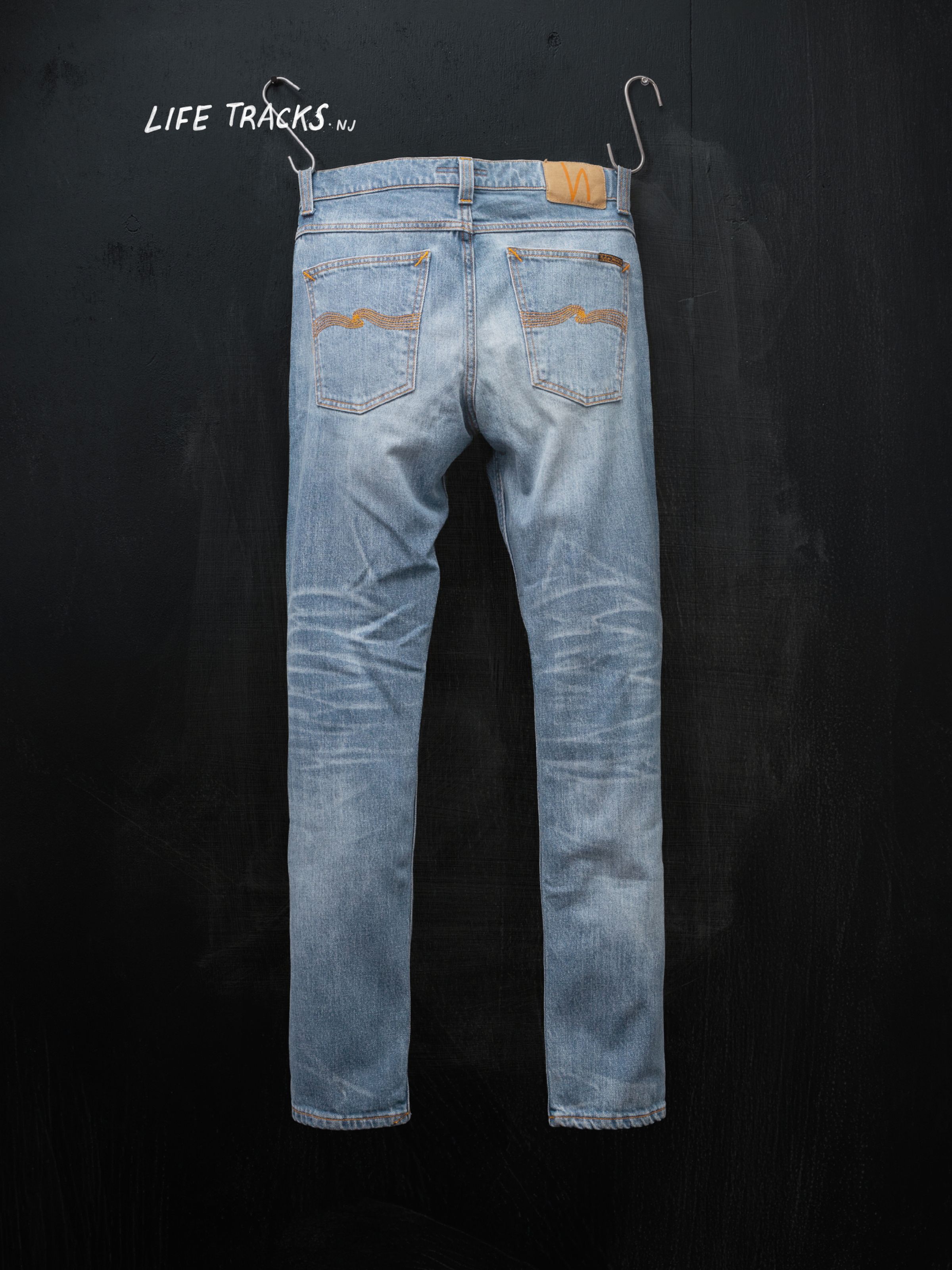 Nudie Jeans Lean Dean Hidden Tracks, men's jeans from the Life Tracks collection, hanging from the back against a black wall.