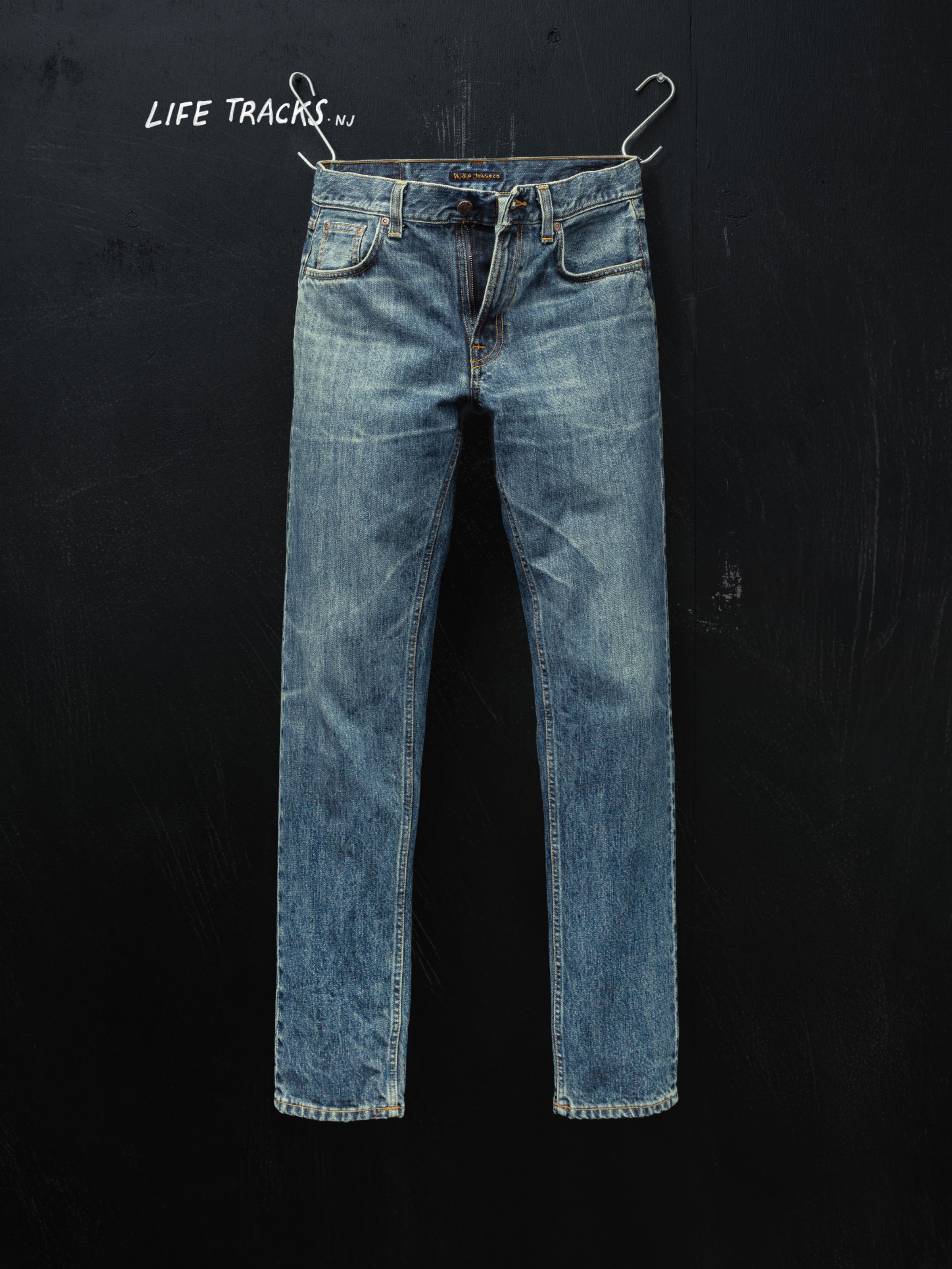 Nudie Jeans Gritty Jackson Thriller Tracks, men's regular fit jeans hanging against a black wall.