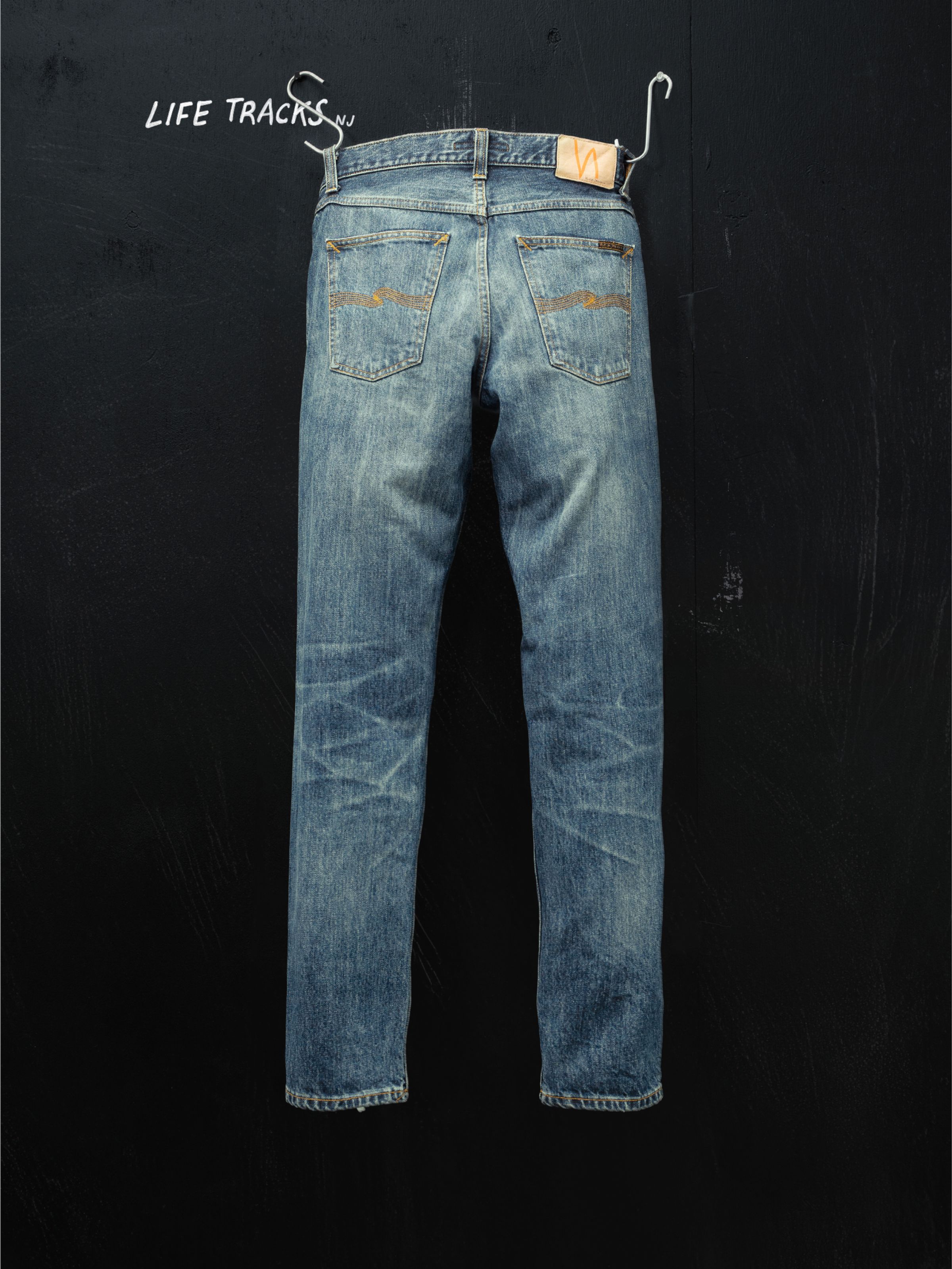 Nudie Jeans Gritty Jackson Thriller Tracks, men's regular fit jeans shown from the back hanging against a black wall.