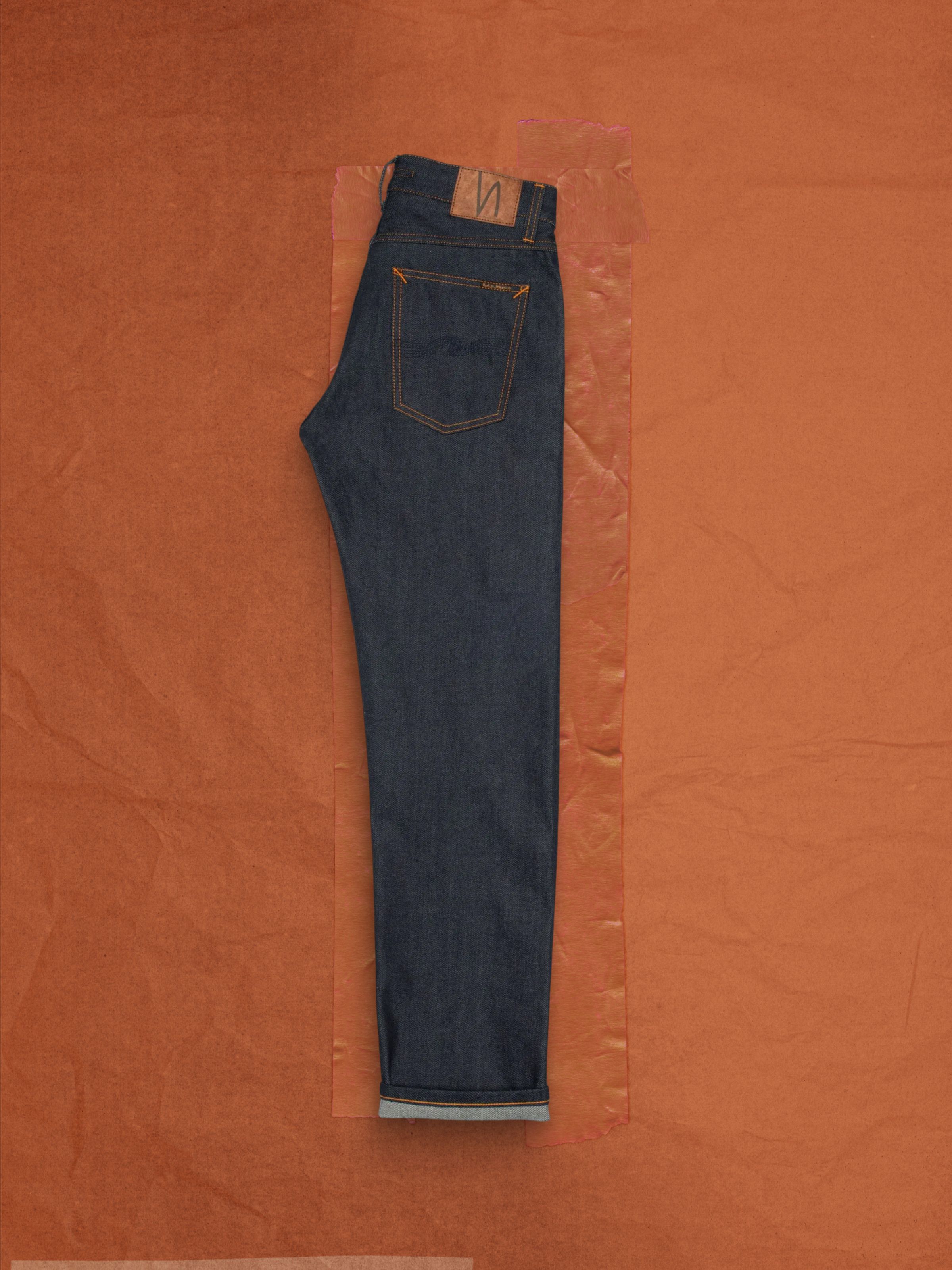 Nudie Jeans Gritty Jackson Dry Dusk Selvage, men's regular fit jeans, folded and laid flat on a brown background.