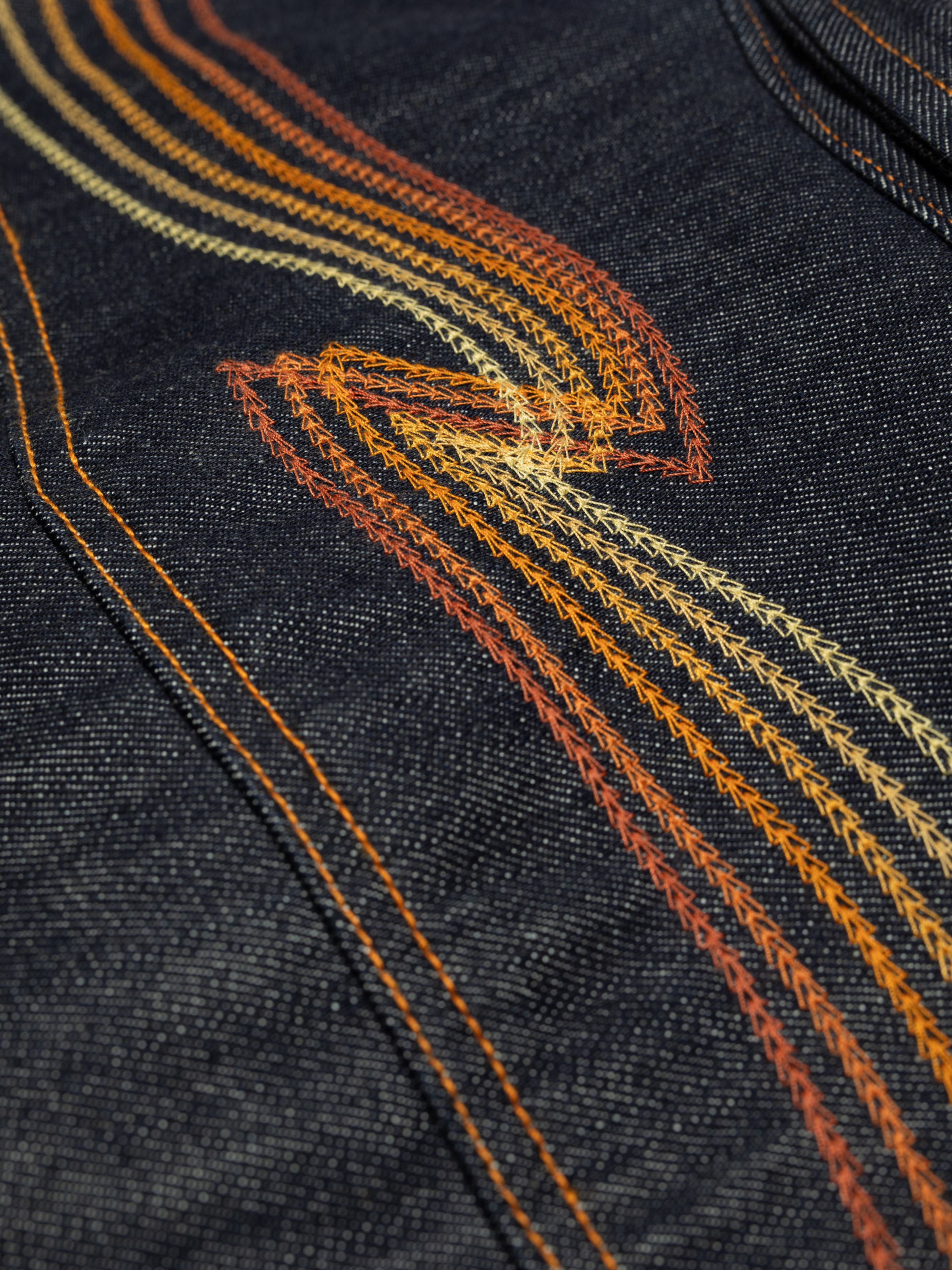 Nudie Jeans Conny Denim Jacket Sunburns, a close-up of the orange gradient back yoke embroidery on the dry blue denim.