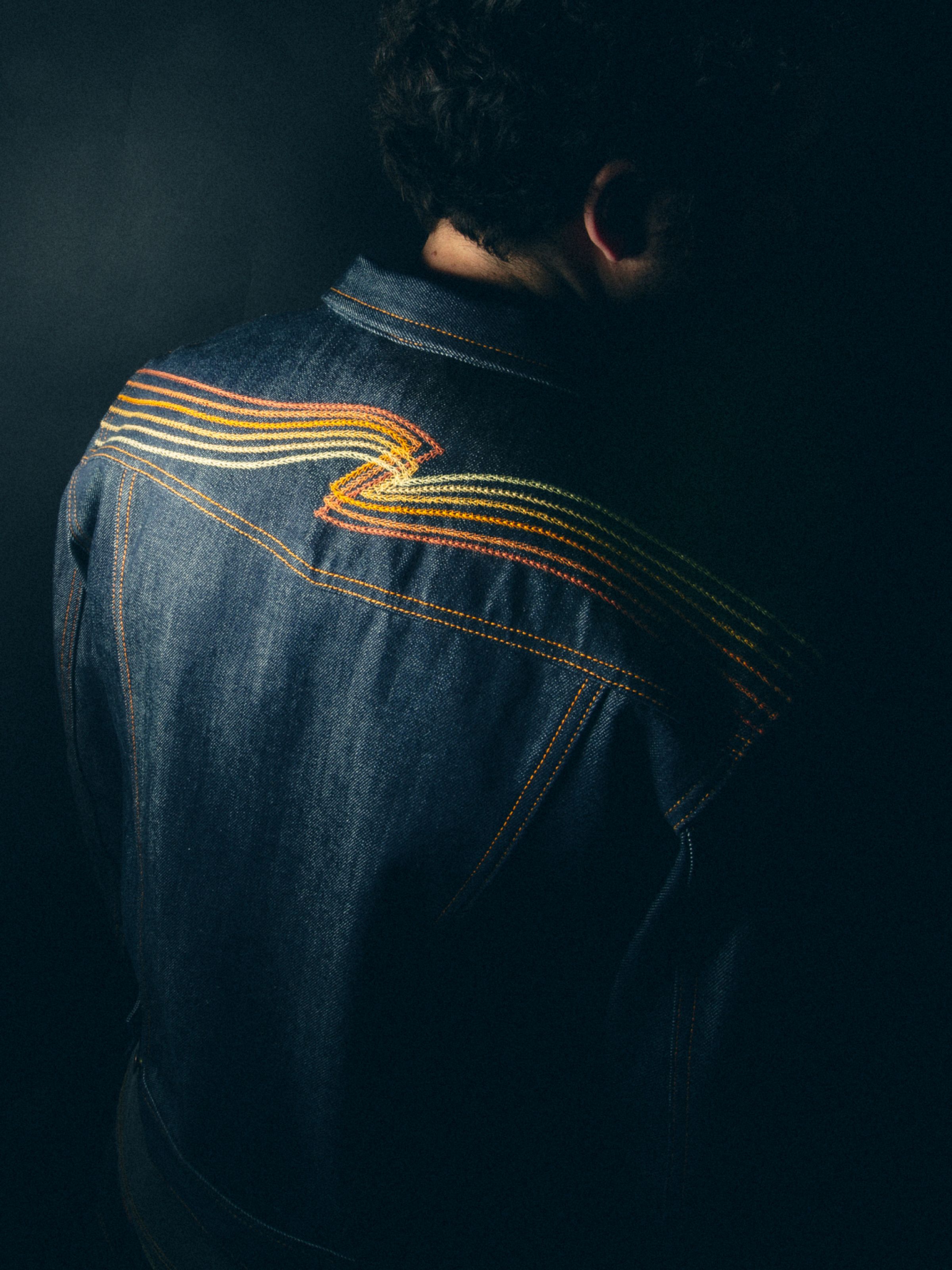 Nudie Jeans Conny Denim Jacket Sunburns, a men's slim fit denim jacket, showing a close-up of the back embroidery on a model.