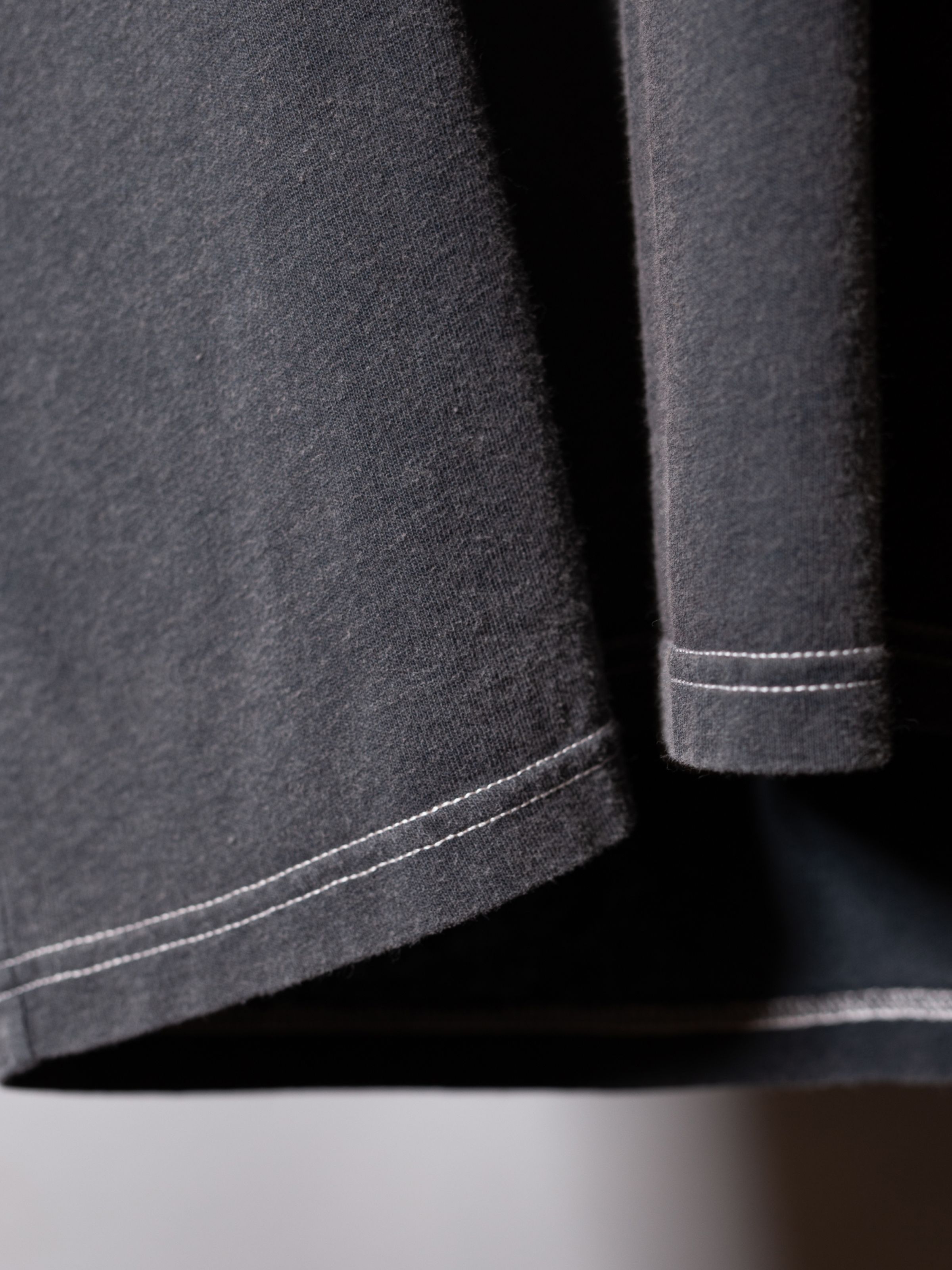 Nudie Jeans Koffe Scratched Tracks T-Shirt Antracite, a men's t-shirt, showing a detail of the hem with off-white stitching.