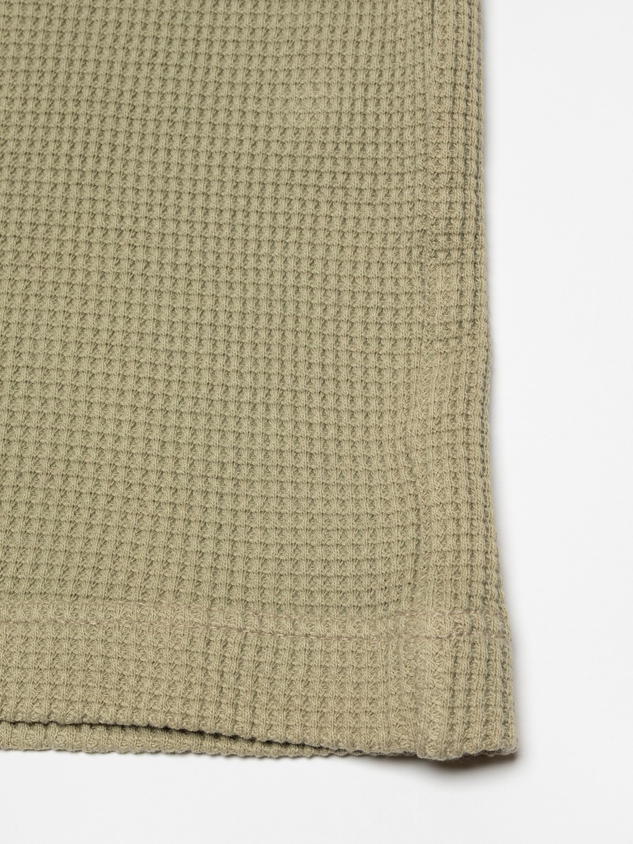 Nudie Jeans LS Henley Waffle T-Shirt in Desert, a men's top, in a close-up shot highlighting the waffle knit fabric and hem.