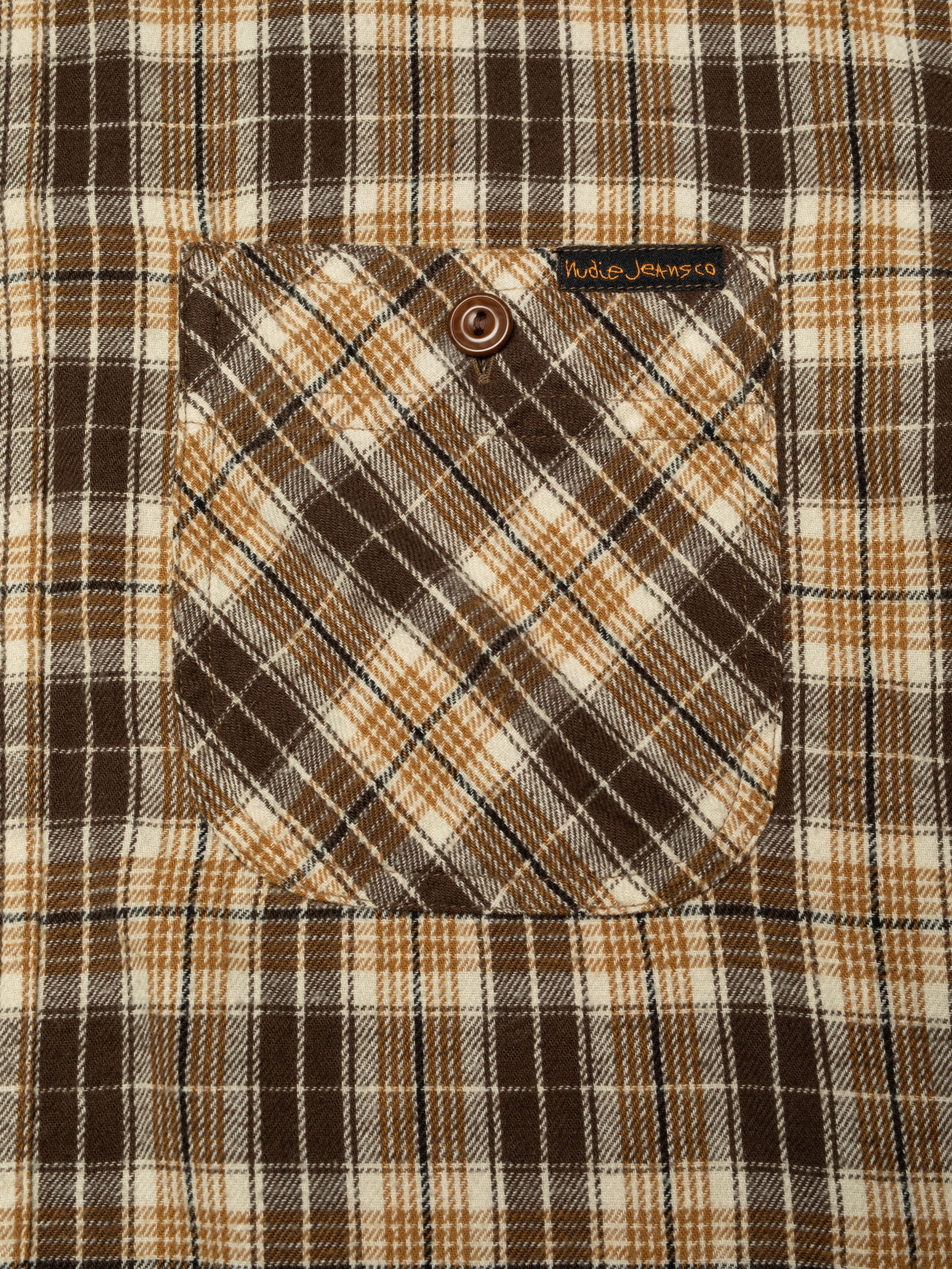 Nudie Jeans Julian Worker Shirt Check Brown, a men's shirt in brown plaid, shown in a close-up of the chest pocket.