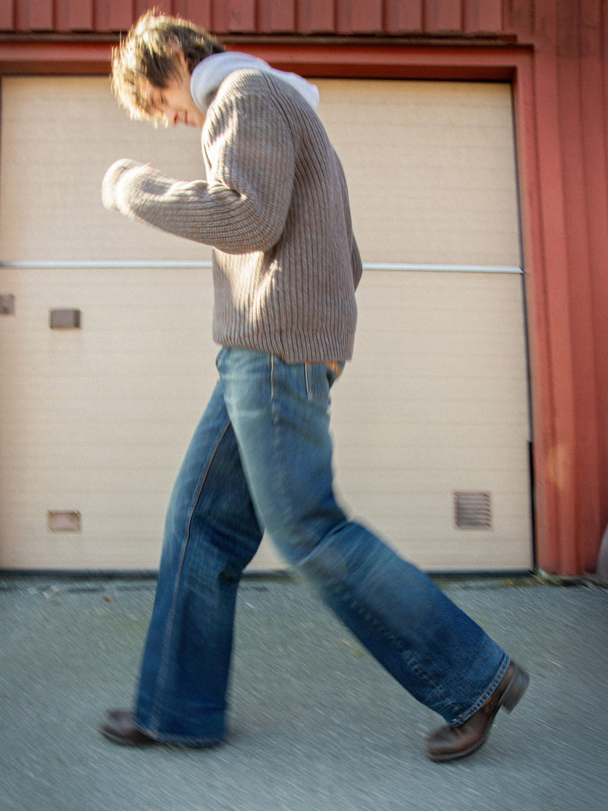 Nudie Jeans August Chunky Crew Neck Knit in Brown, a men's chunky knit sweater, worn by a model walking from the side.