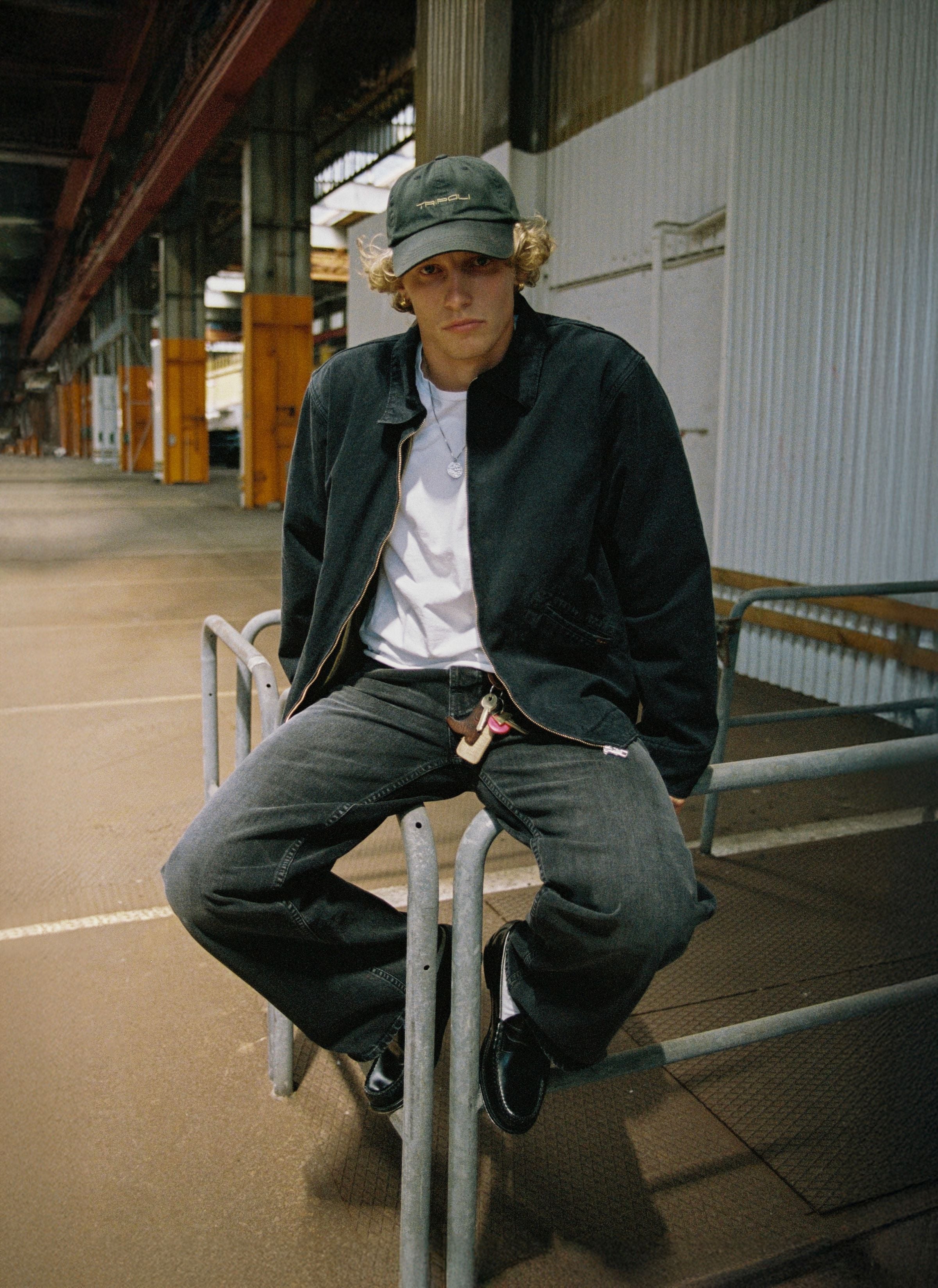Nudie Jeans Blake Zip Jacket Duck Canvas in Schwarz, Herren-Arbeitsjacke, getragen von einem Model auf einem Geländer.
