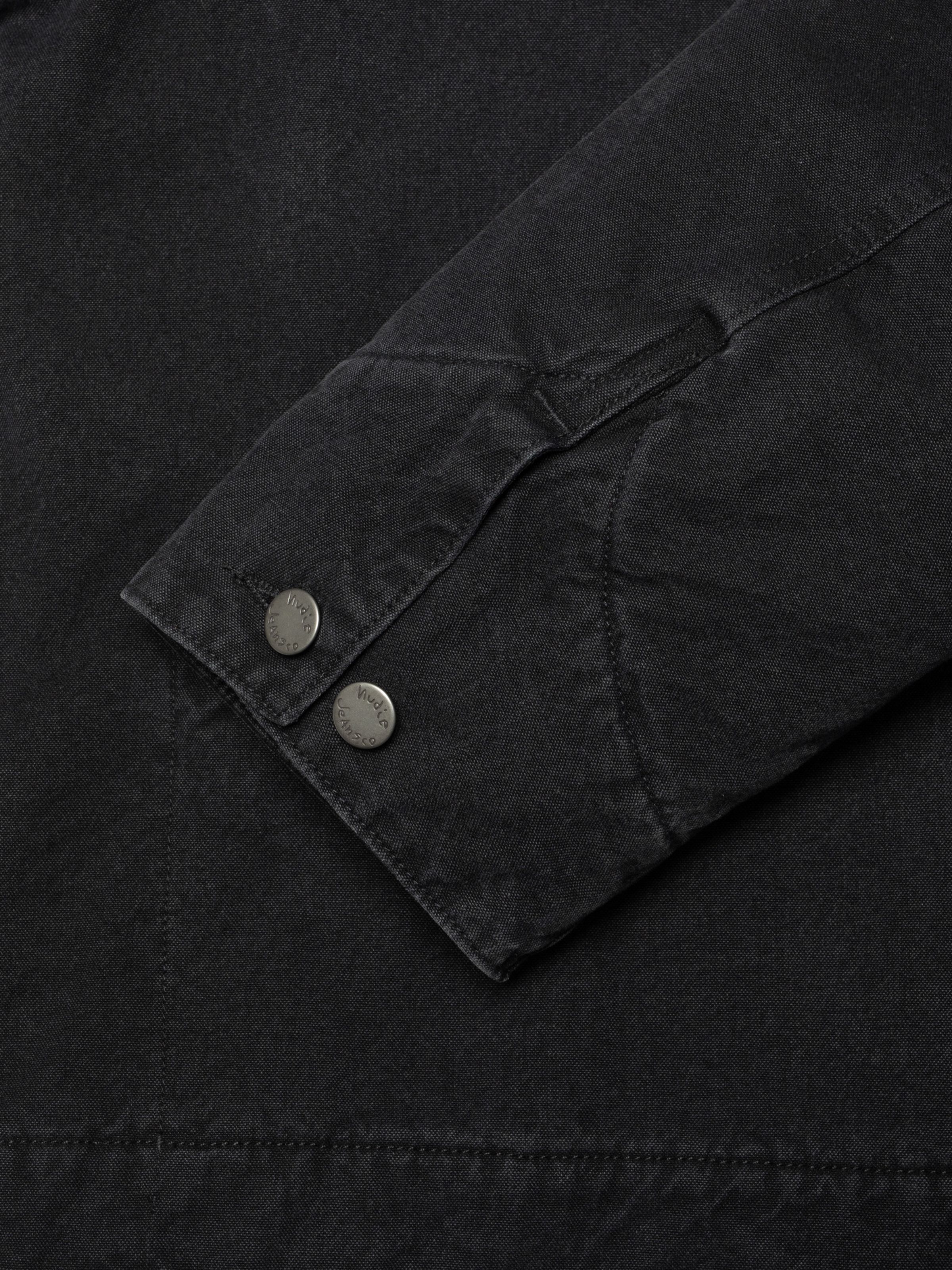 Nudie Jeans Blake Zip Jacket Duck Canvas in black, showing a close-up detail of the sleeve cuff with antique silver buttons.