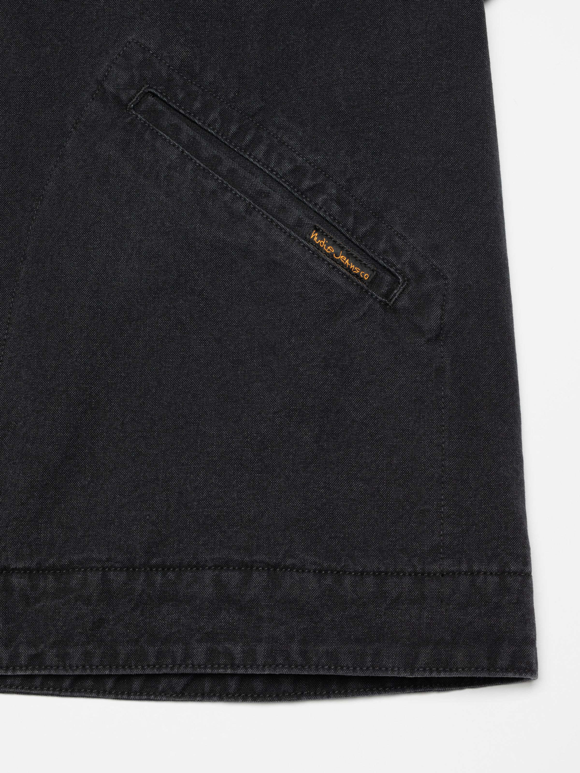 Nudie Jeans Blake Zip Jacket Duck Canvas, a men's jacket in black, showing a close-up of the welt pocket and logo tag.