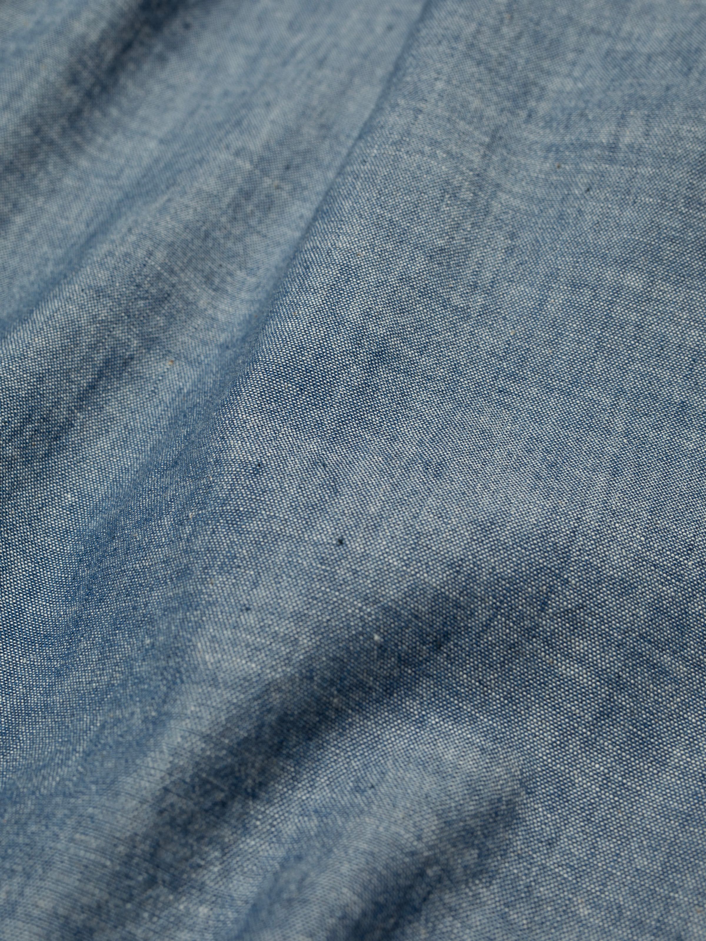 Nudie Jeans Daisy Chambray Western Shirt, a close-up detail shot of the blue Turkish chambray fabric.
