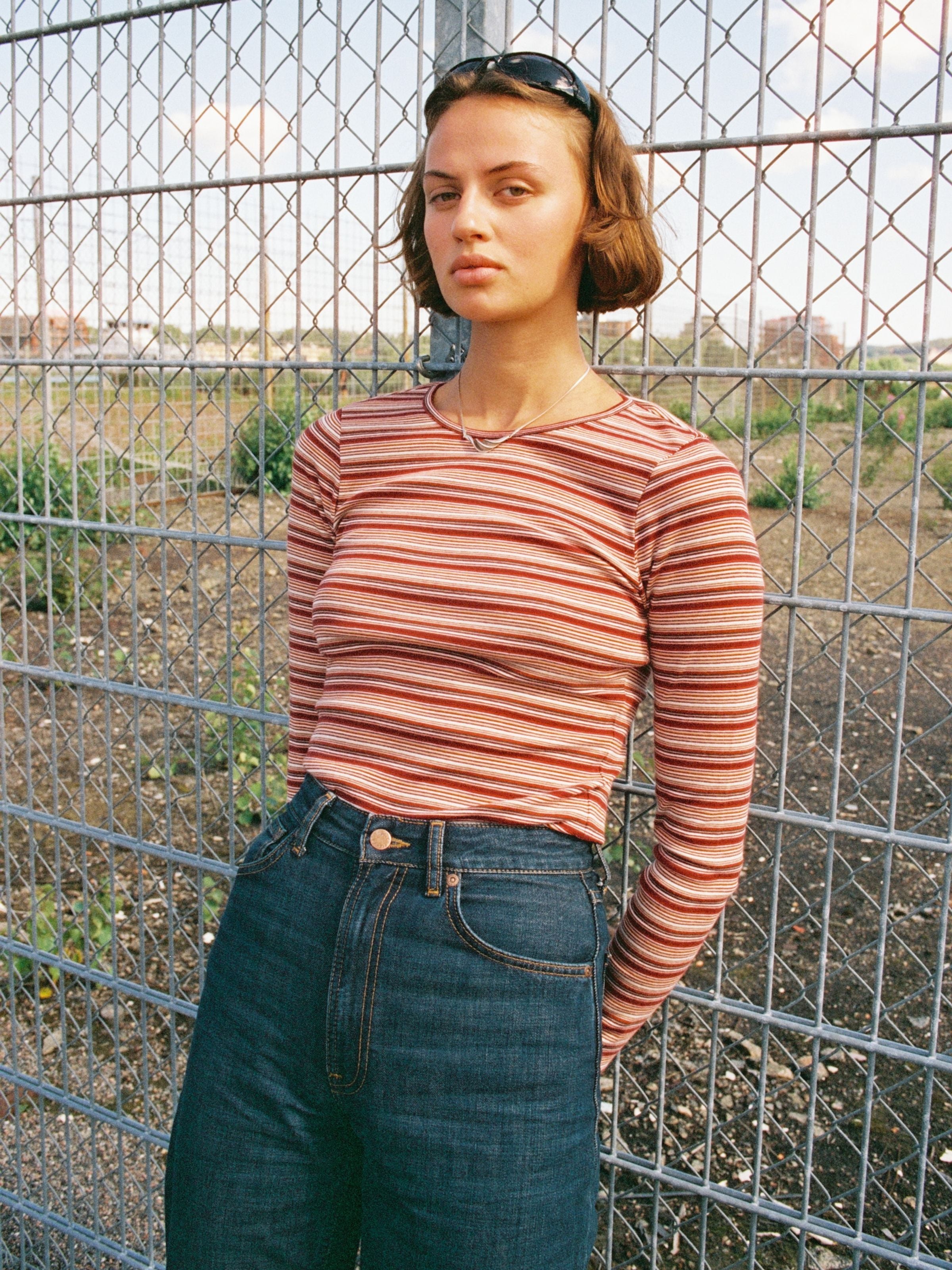 Nudie Jeans Jessy LS T-Shirt Striped Rib in Wine, ein gestreiftes Damen-Langarmshirt, von einem Model im Freien getragen.